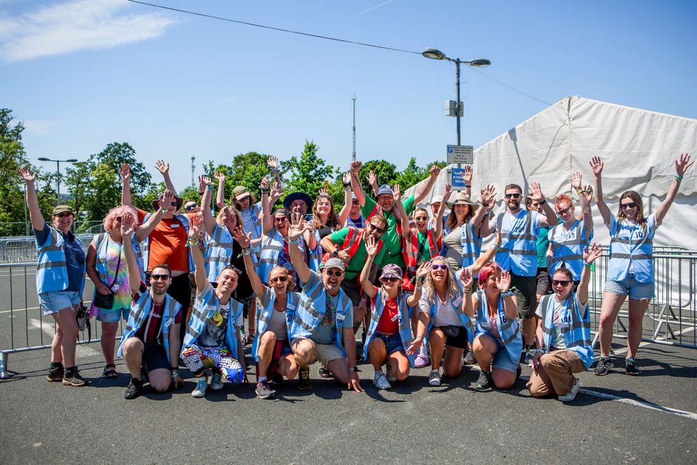 Large group of fans in blue shirts celebrating outdoors at a summer festival, cheering with arms raised.