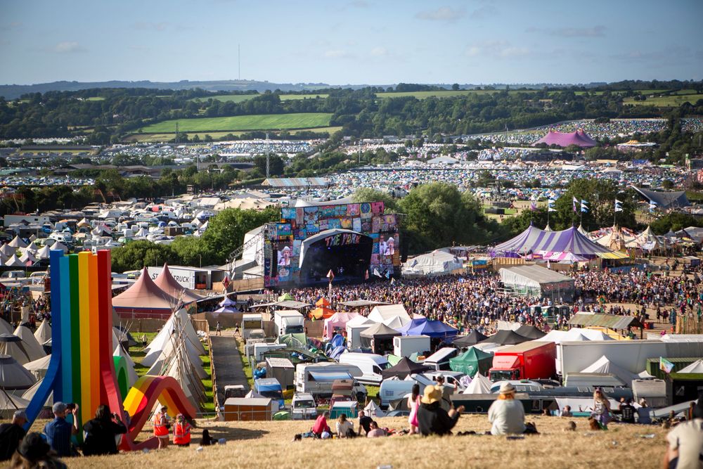 Aerial view of a large outdoor music festival with colorful tents, a main stage, and crowds on a sunny day.