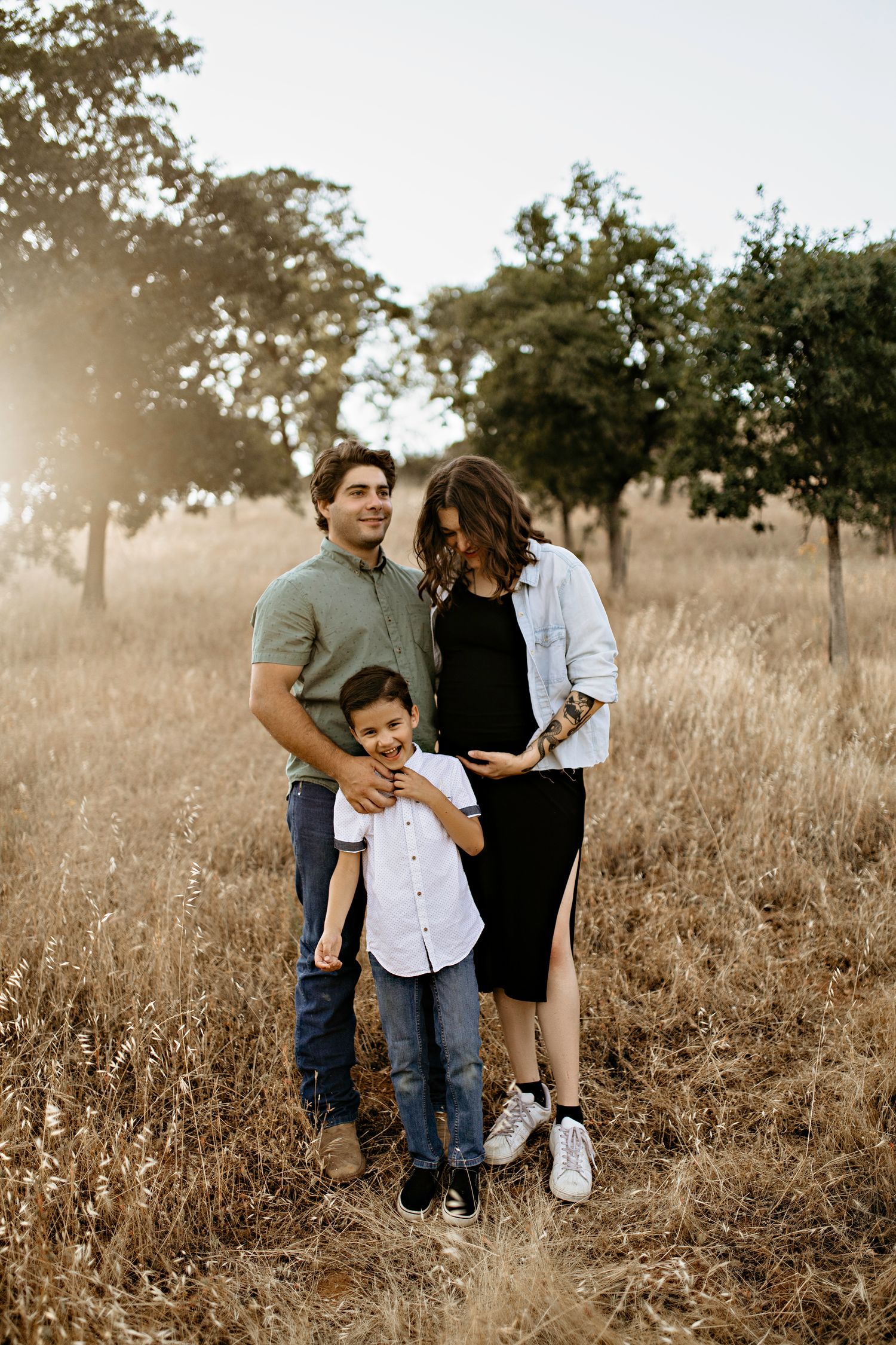 El Dorado Hills Family of three posing together in a sun-drenched field with tall dried grass and trees in the background.