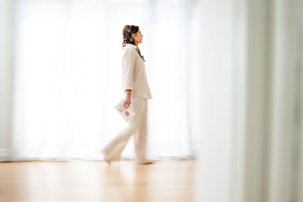 A person in white clothing walks through a bright minimalist interior with white walls and curtains.