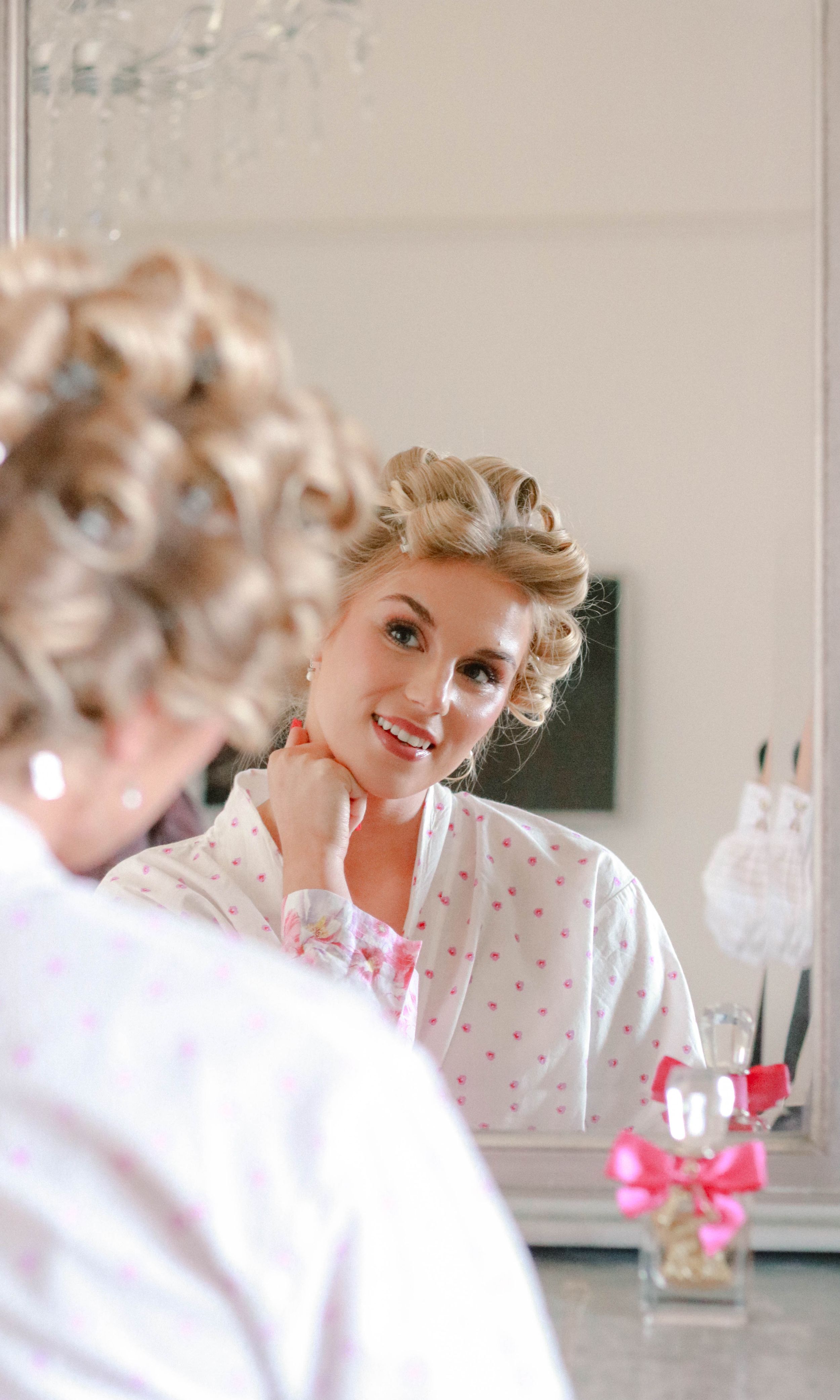 Vintage style portrait of someone in white clothing with retro hairstyle smiling in a bright, airy setting.