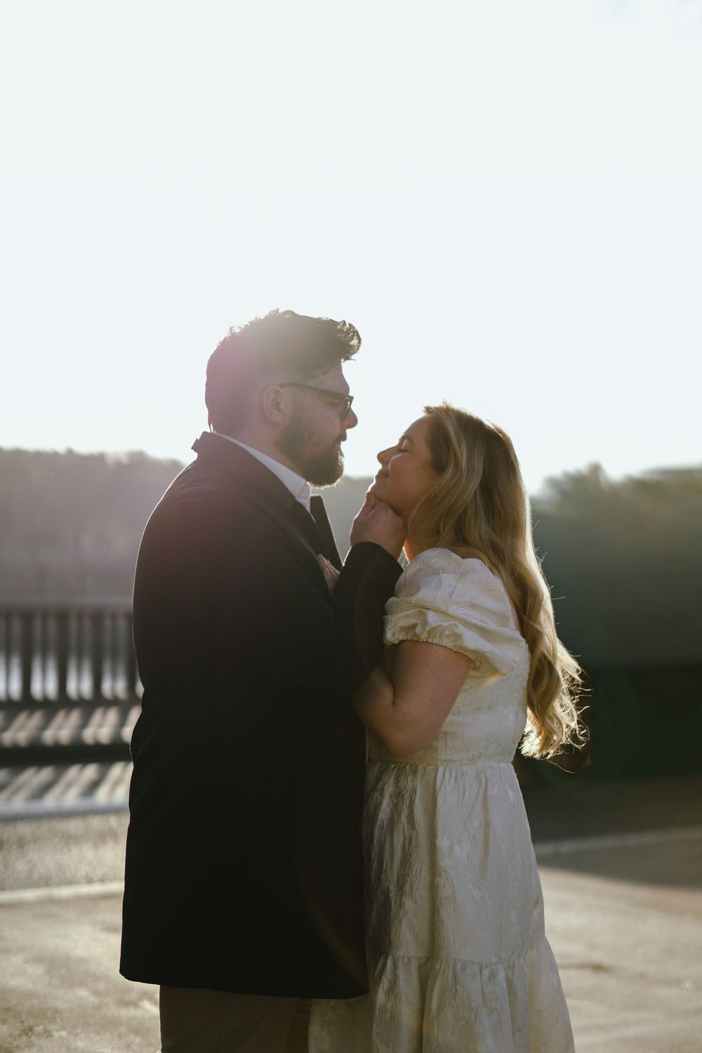 A couple shares a romantic moment outdoors, backlit by golden sunlight, as the man gently touches the womans chin.