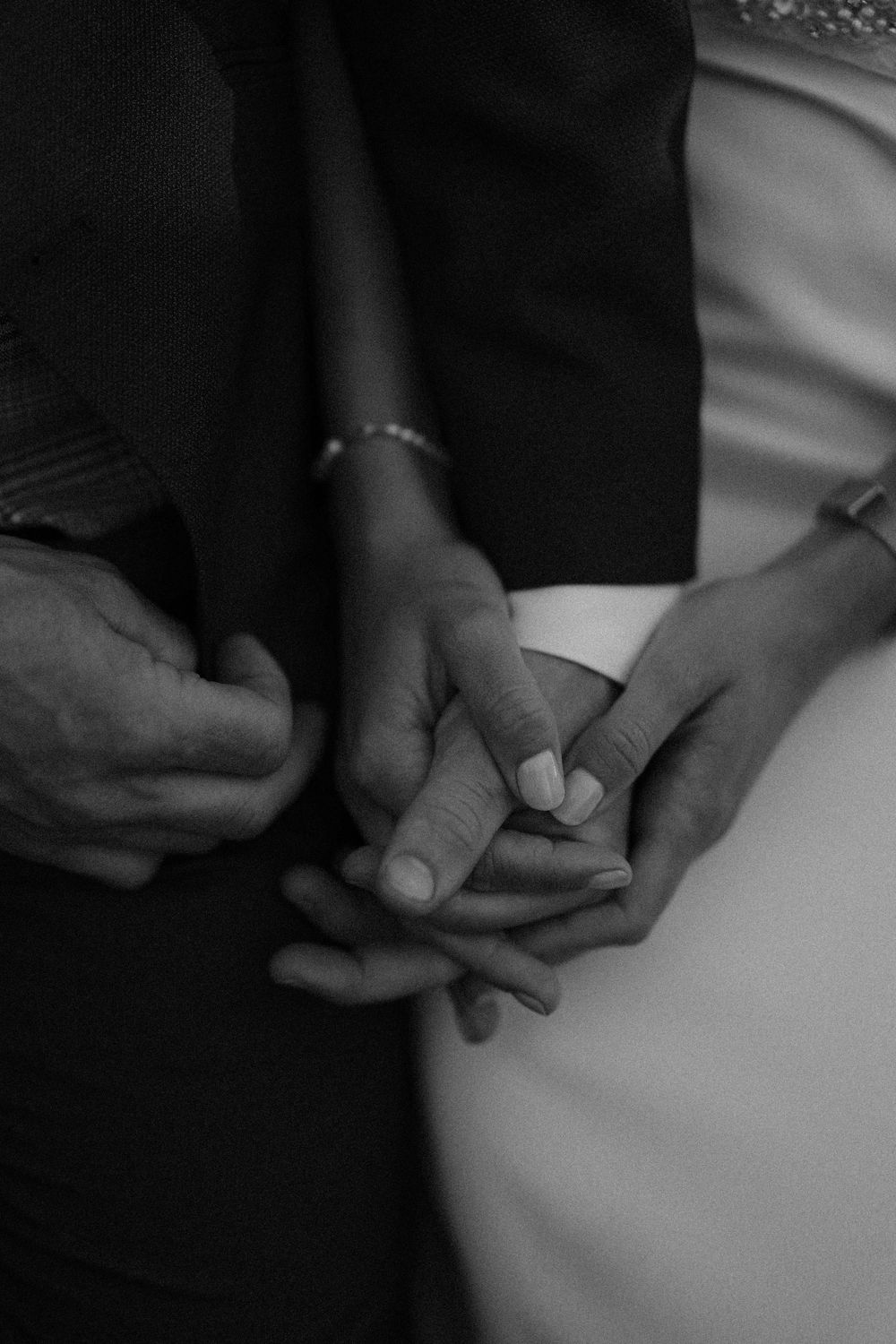 Black and white close-up photo of hands clasped together intimately in a tender romantic moment.