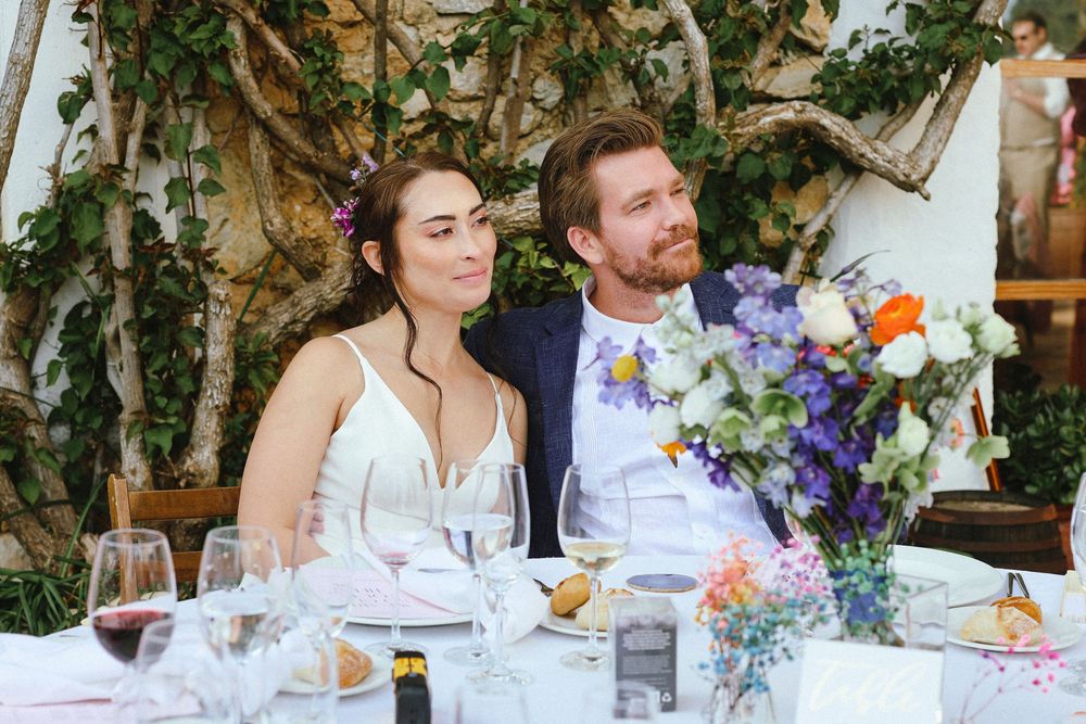 Elegant garden wedding reception features a long banquet table adorned with colorful floral centerpieces and wine glasses.