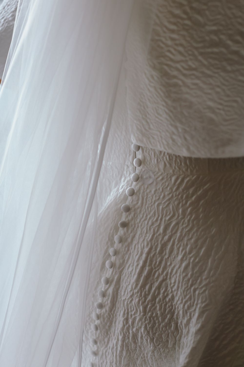 Close-up detail of delicate button closures on a textured white wedding dress with flowing fabric.