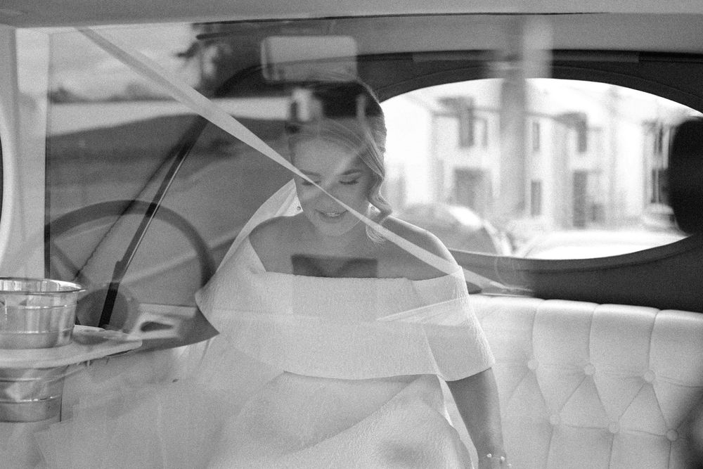 Black and white photograph showing interior of a luxury car with tufted leather upholstery visible through a window.