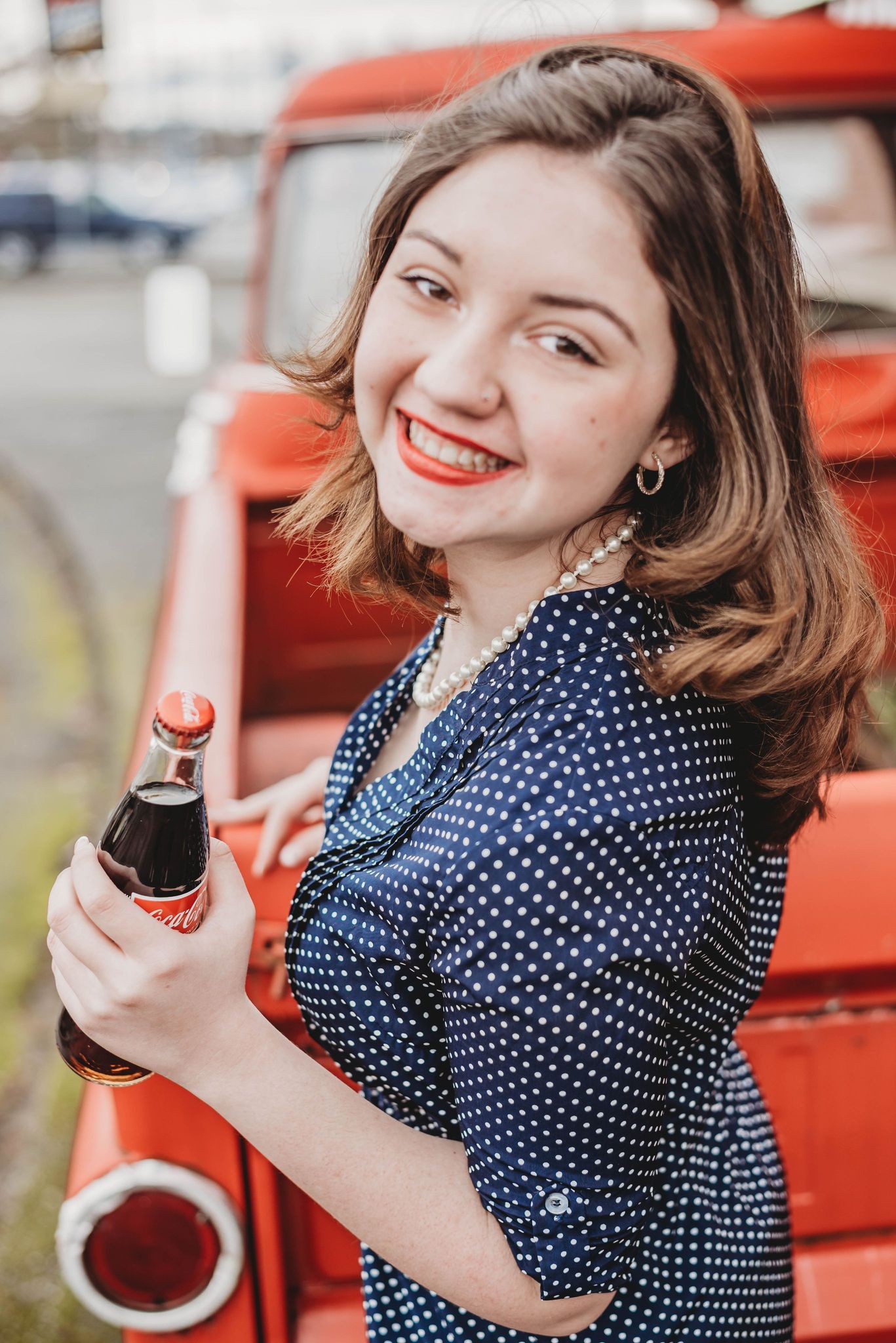 A retro-styled photoshoot featuring someone in a polka dot dress with a vintage red backdrop.