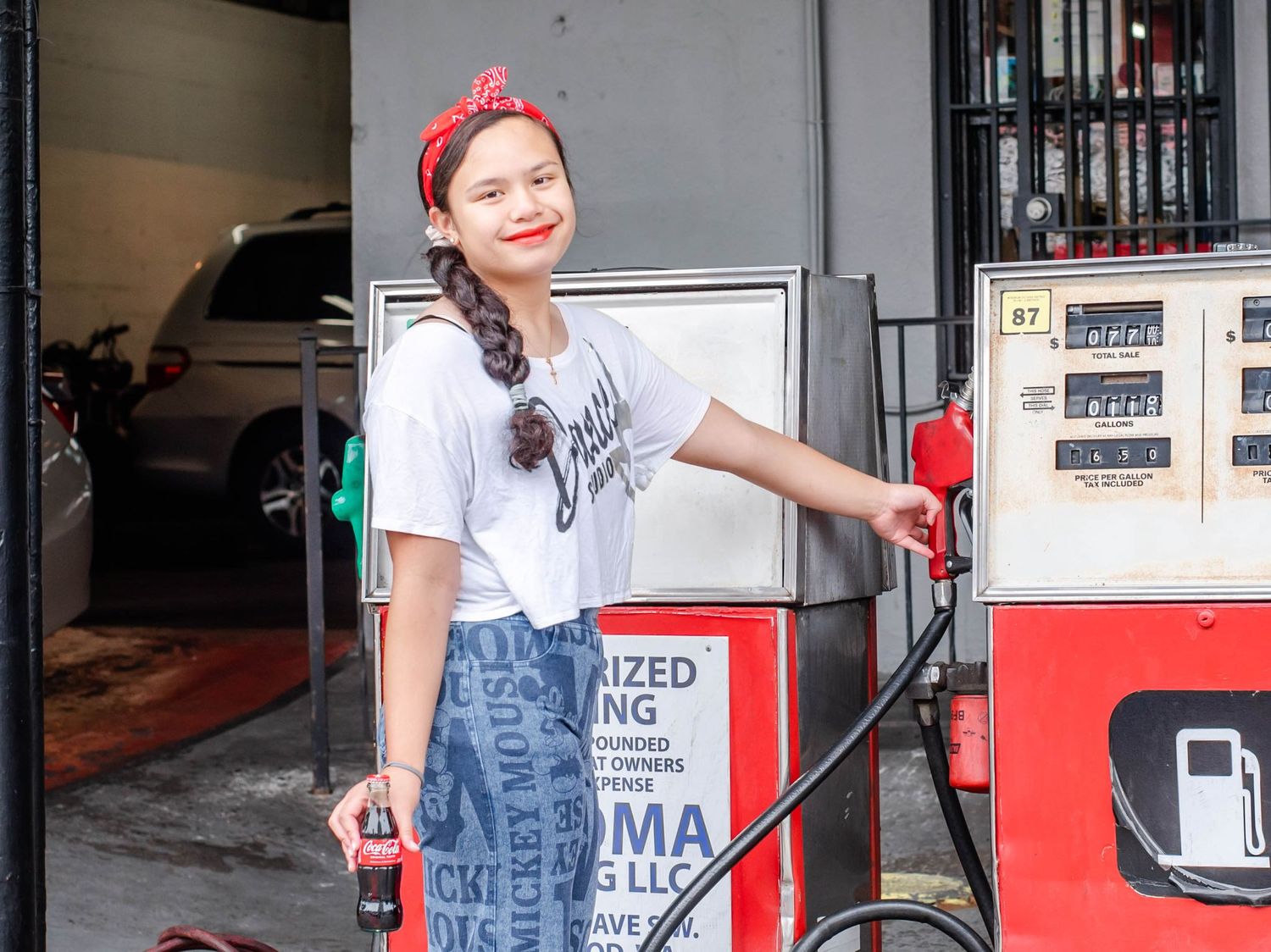 Vintage gas station setting with a person sitting on a folding chair in denim overalls.