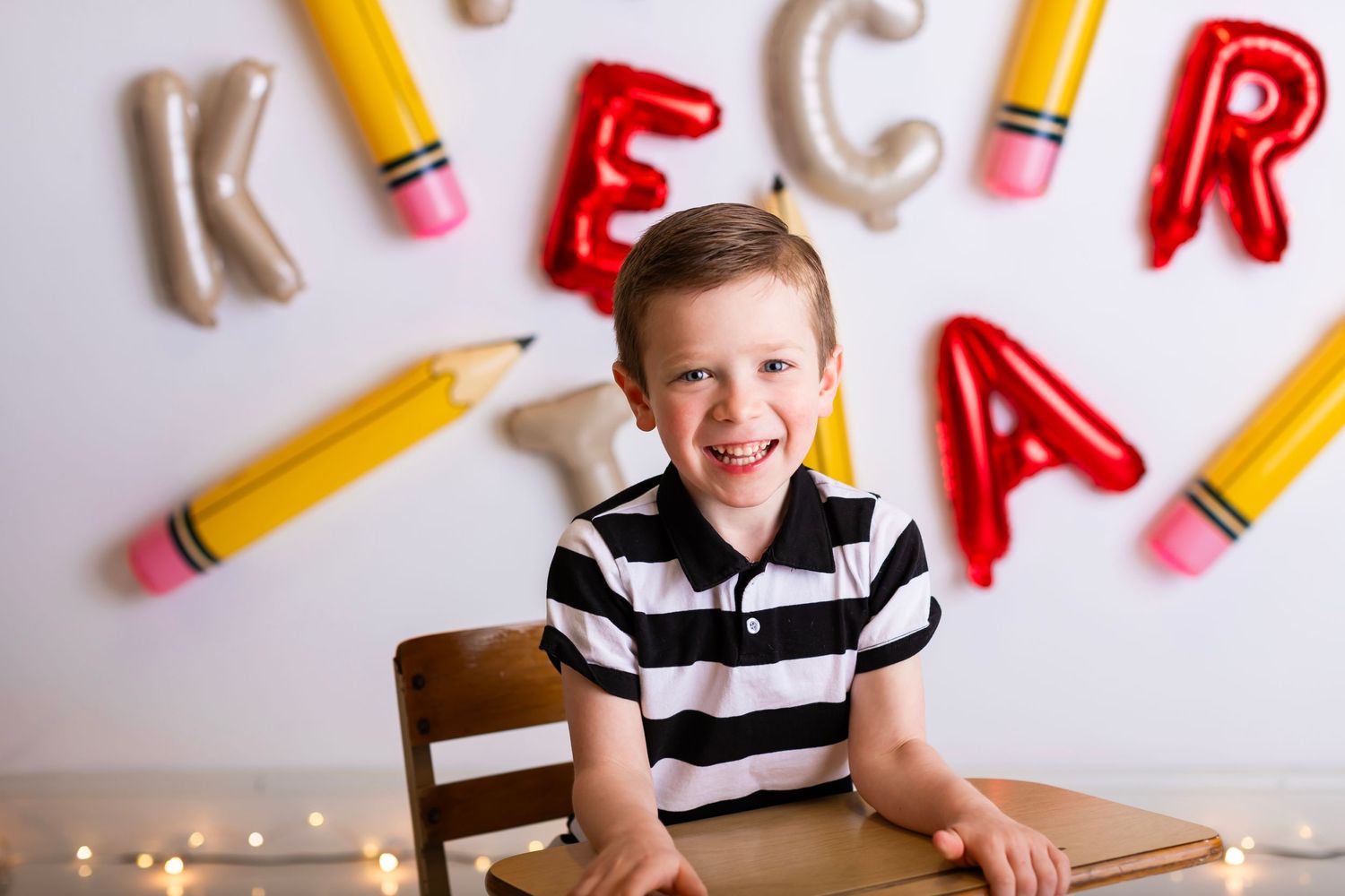 Happy student sitting at desk with alphabet letters and pencil decorations on wall.