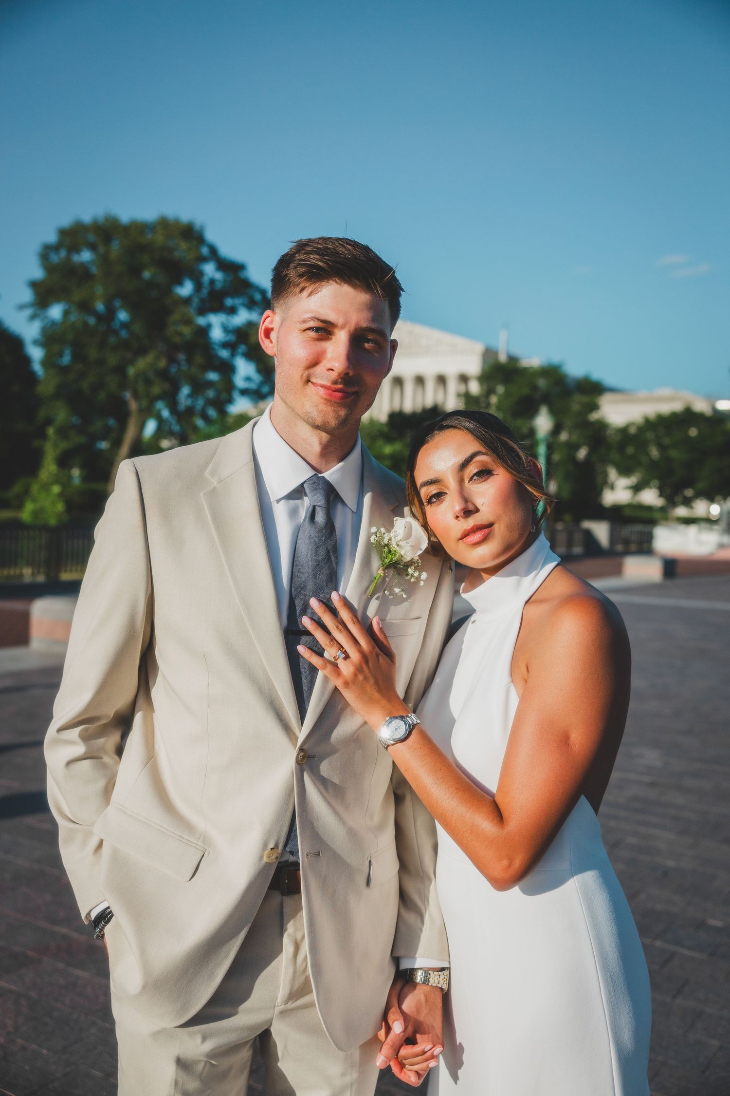 Elegant couple in white and beige formal attire posing outdoors by Capitol building.