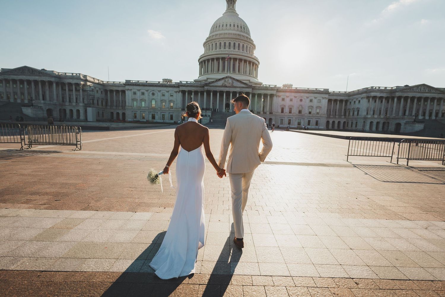 Wedding couple holding hands walking toward US Capitol building in sunlight.