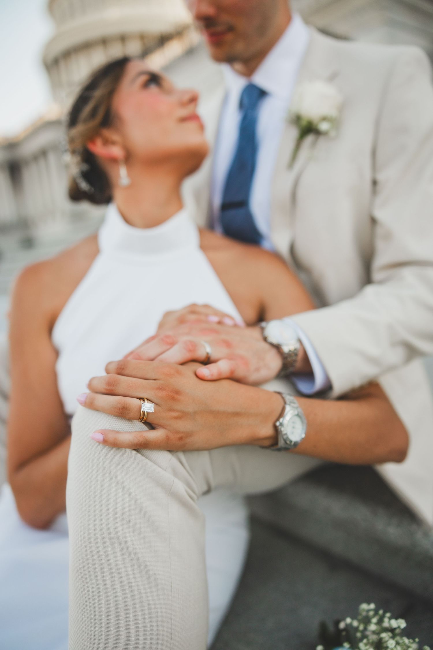 Close up of couple's hands with wedding rings in front of Capitol building.