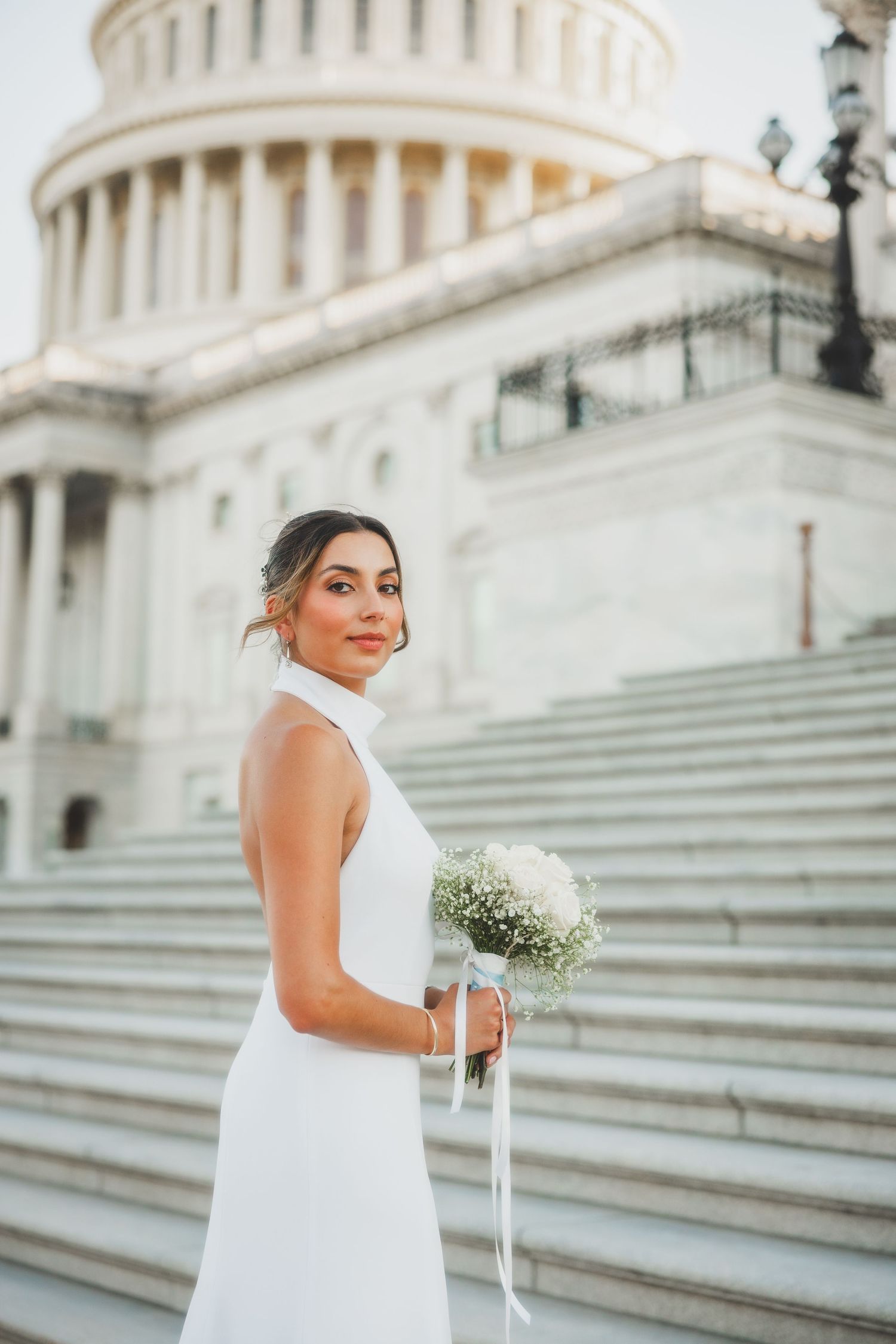 Bride holds white floral bouquet while standing on marble steps of Capitol Building.