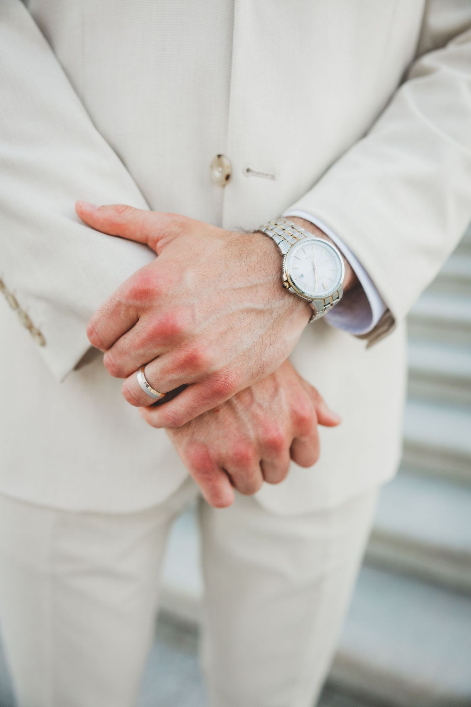 Close-up of hands wearing white suit and silver watch.