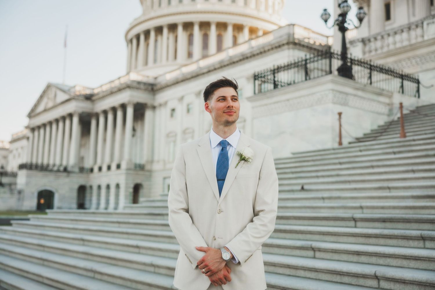 Person in cream suit standing on Capitol building steps with hands clasped.