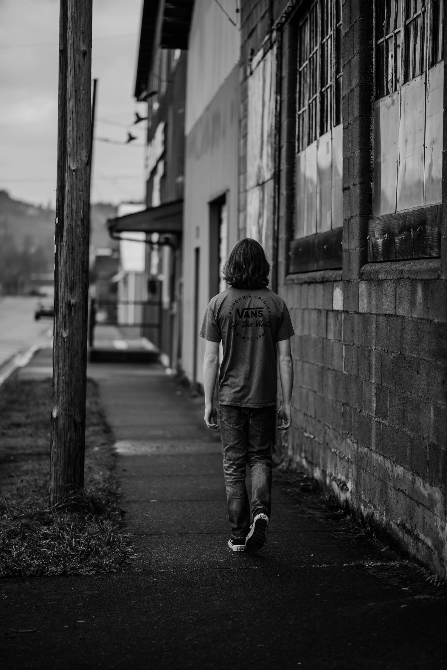 Black and white photo of person walking along urban sidewalk next to building wall.