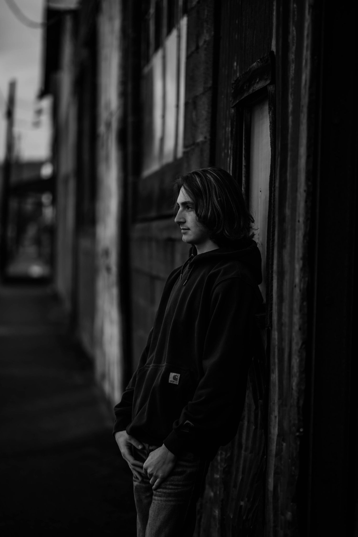 Moody black and white portrait of person in hoodie against urban wall.