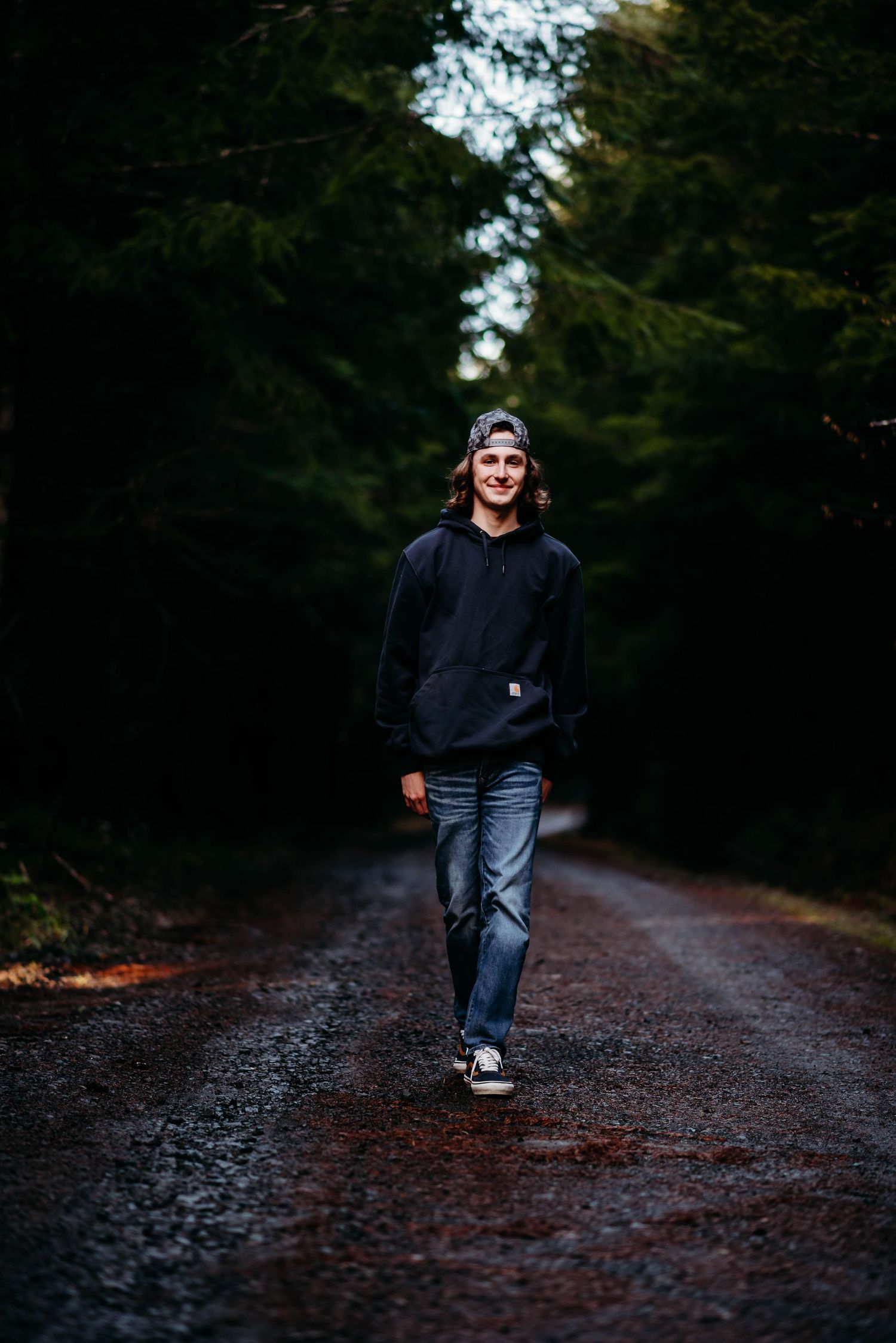 Person in dark clothing walking along forest path in dramatic lighting.