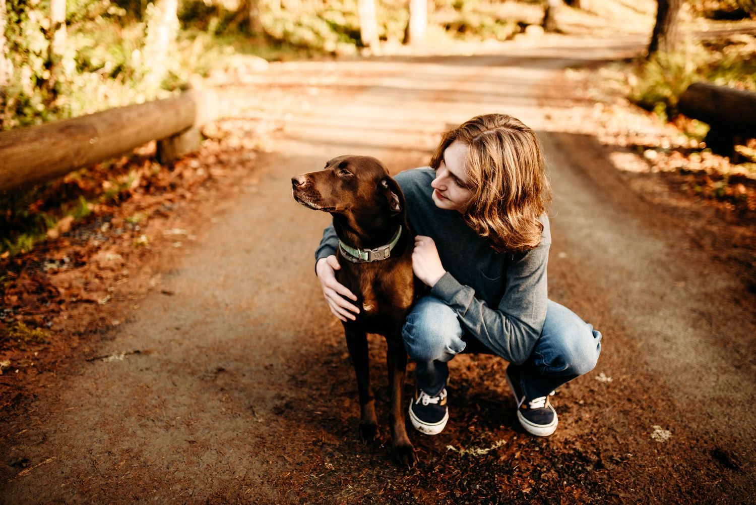 A black dog sits on a leaf-covered path during an autumn photoshoot.