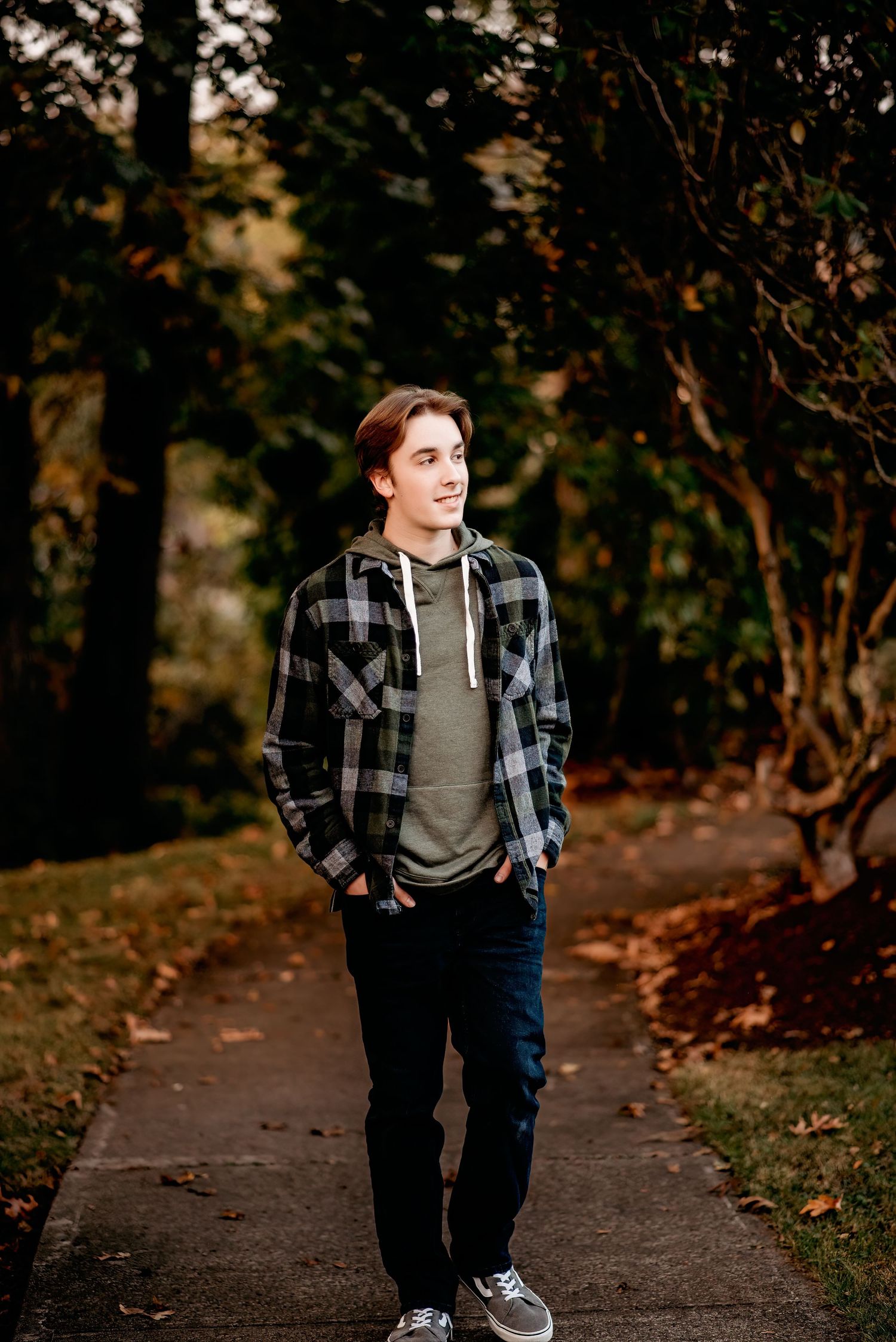 Person wearing plaid flannel and jeans walking on tree-lined path in fall.