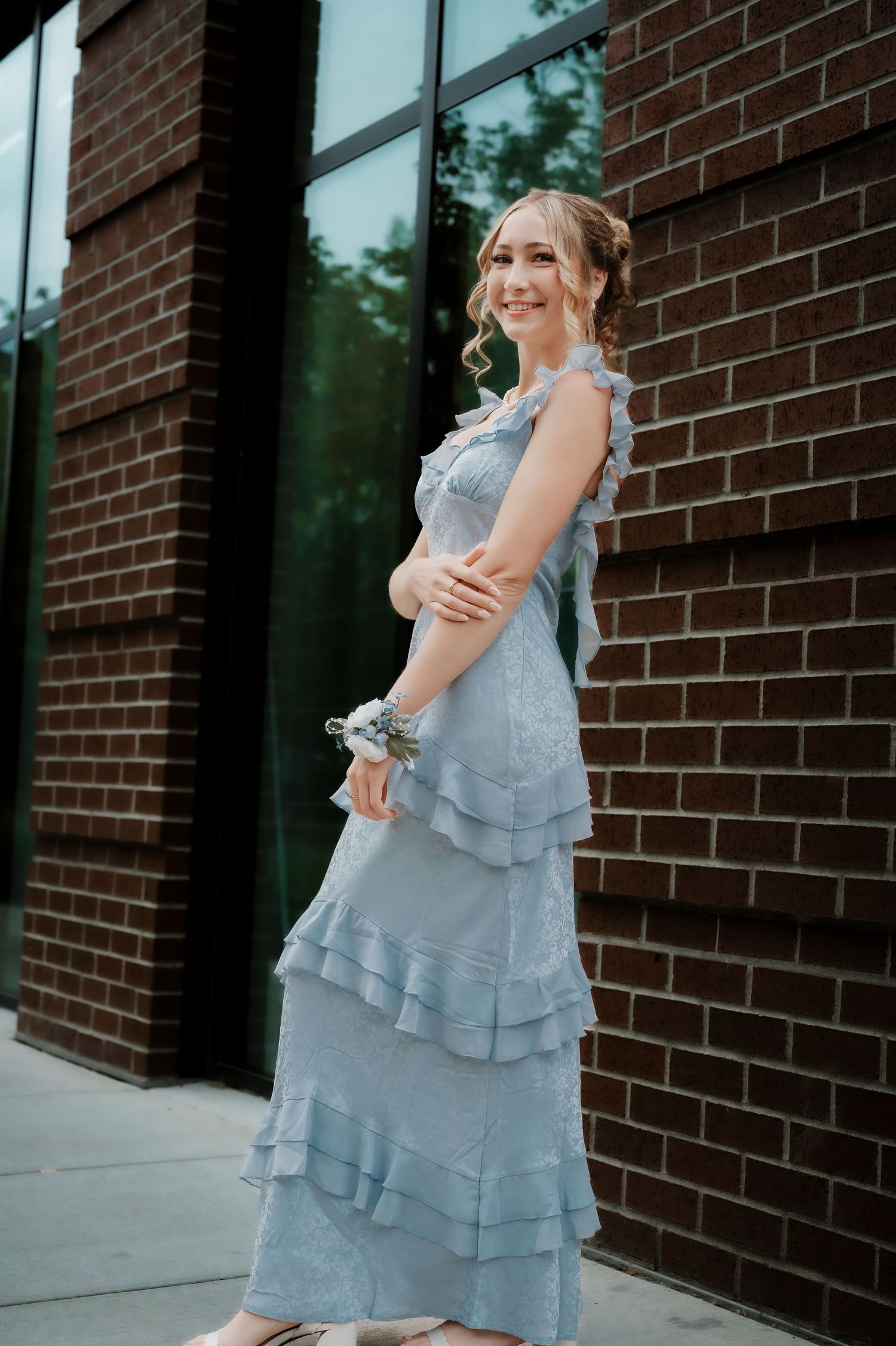 A person in a layered blue dress twirls and dances in front of a brick building.