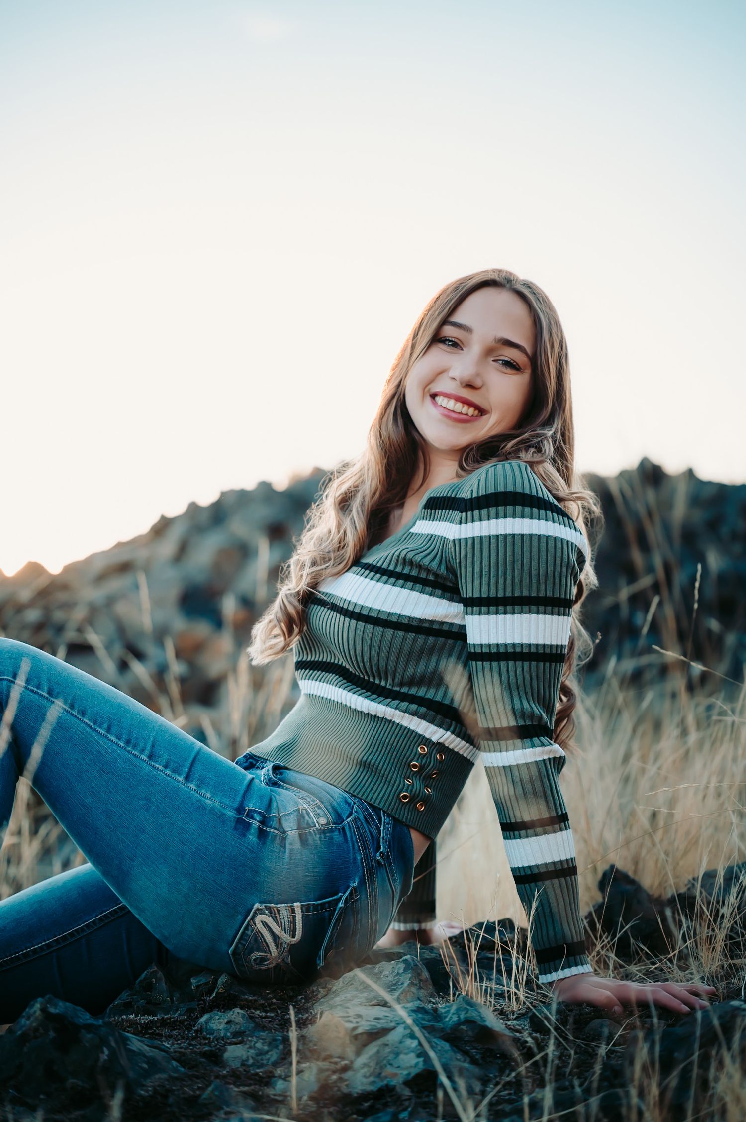 Person in striped sweater and jeans lounging in golden field at sunset.