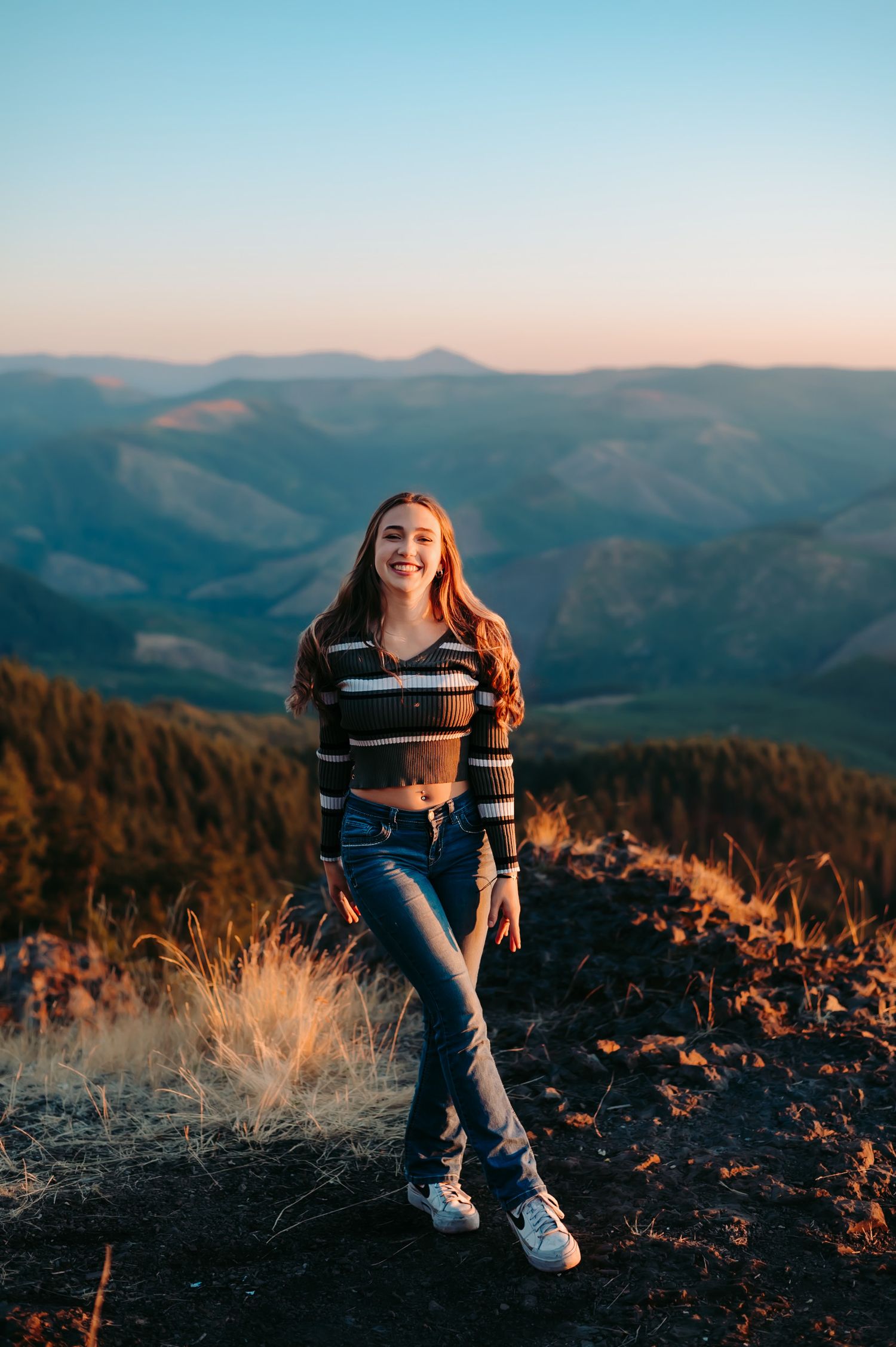 Person in striped sweater sitting on mountain overlook during sunset.