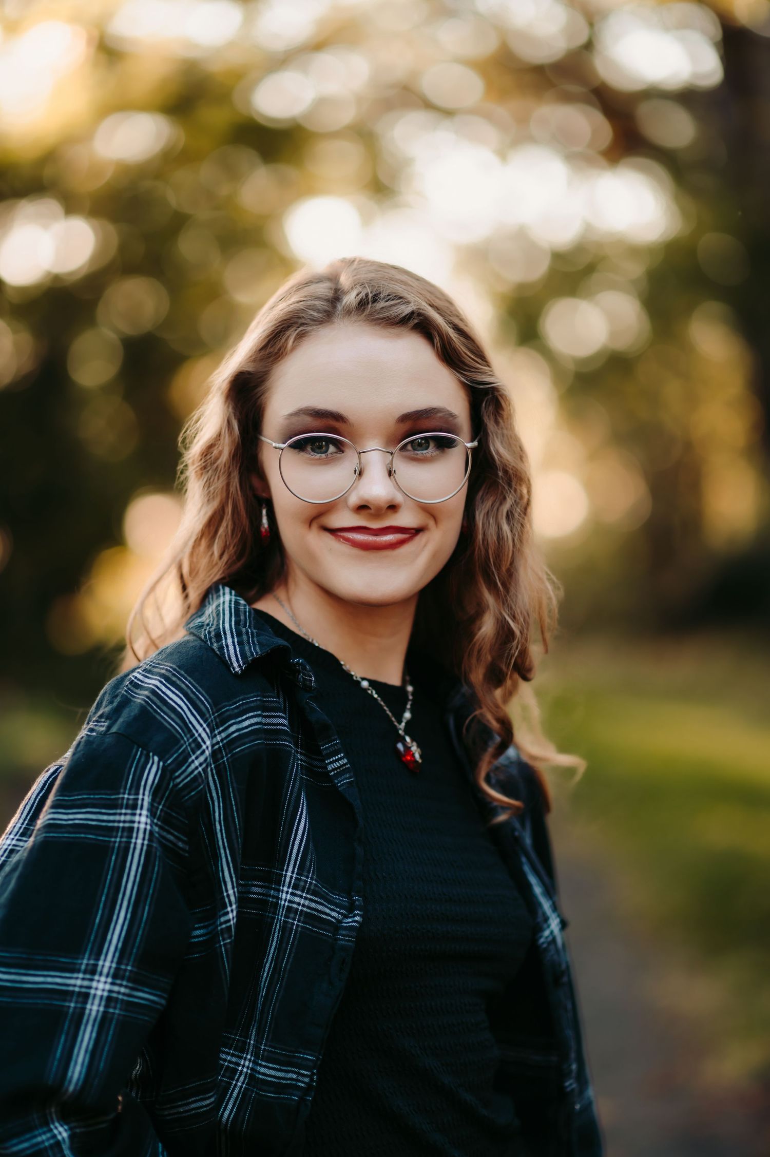 Portrait in natural lighting showing plaid shirt and glasses against blurred autumn background.