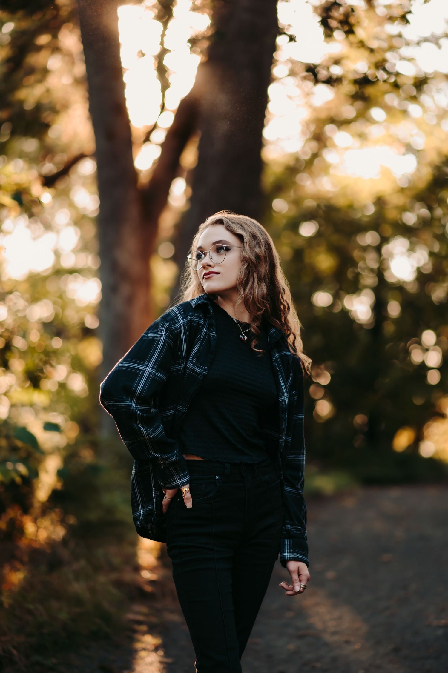 Artistic outdoor portrait with black plaid shirt against golden sunset through trees.