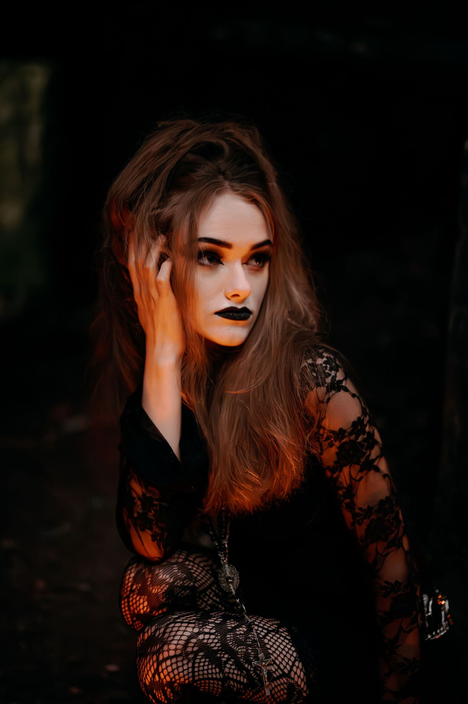 Dramatic portrait in black lace against dark background with orange lighting.