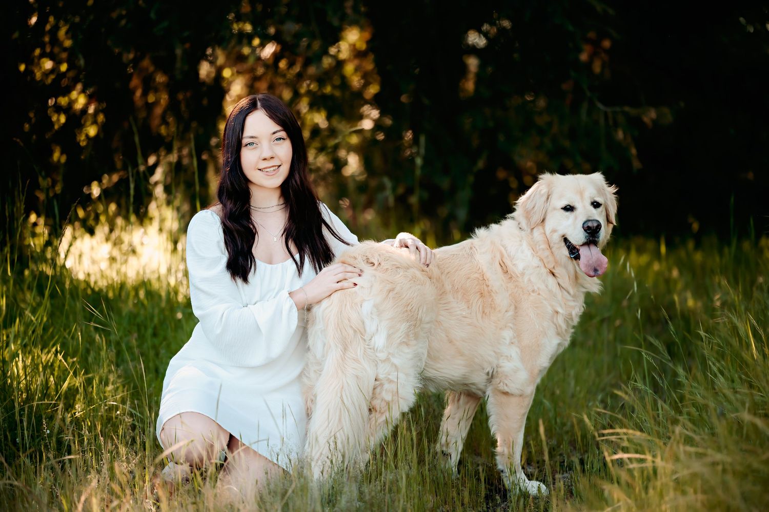 Person in white dress poses with friendly white dog in sunlit meadow.
