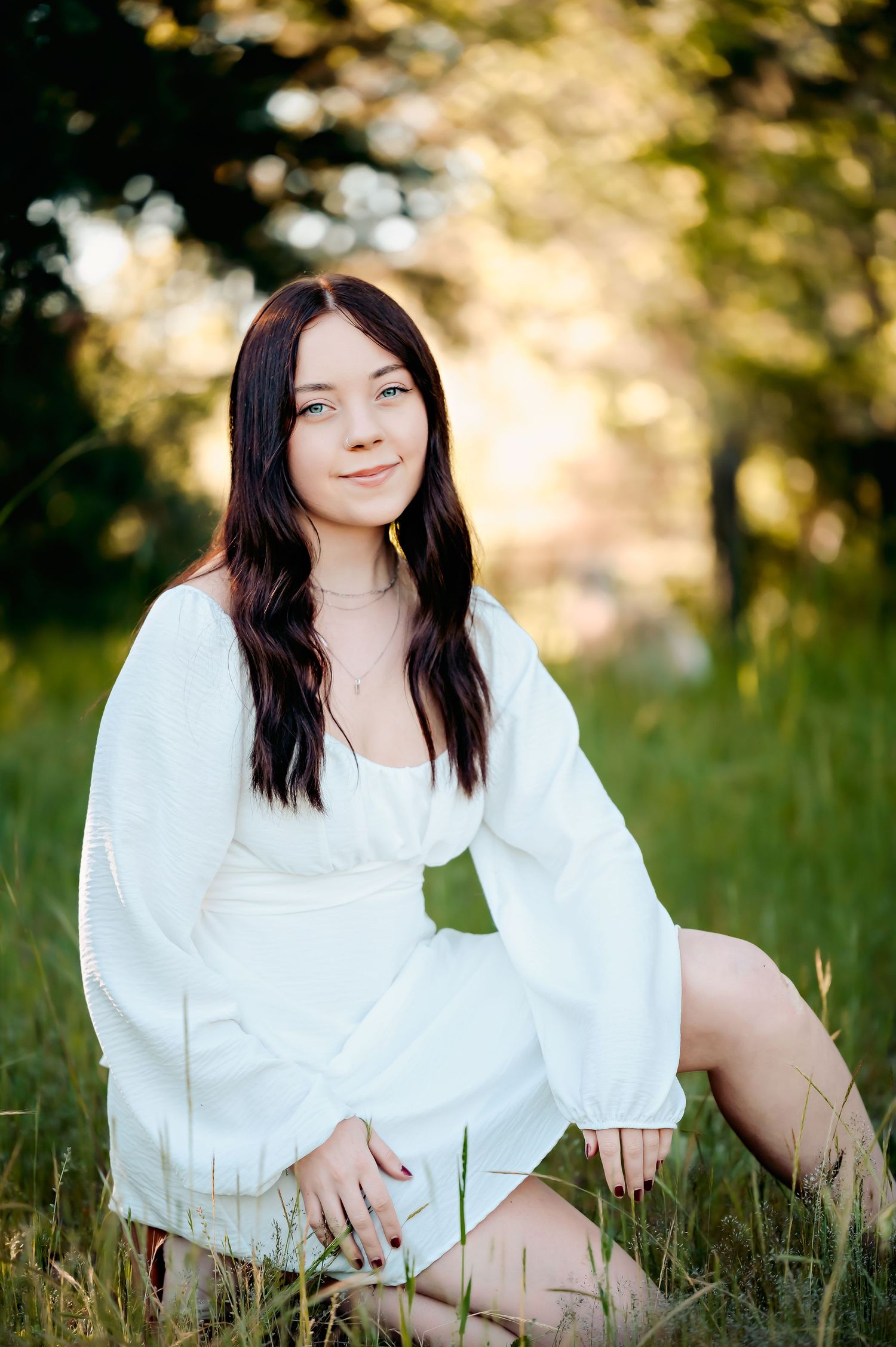 Person in white dress sitting in sunlit meadow during golden hour.