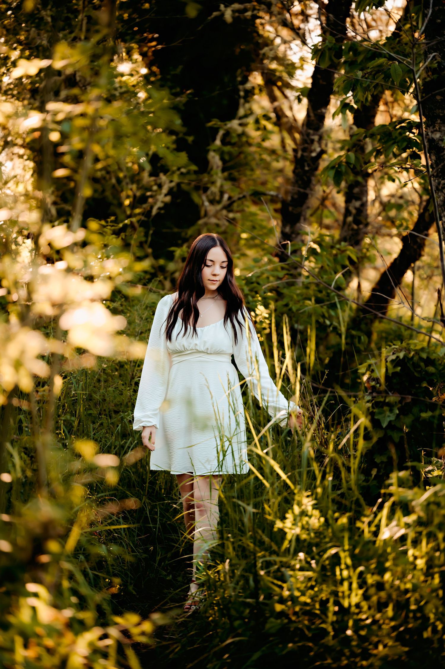 Person wearing white flowing dress walking through sunlit wooded area.
