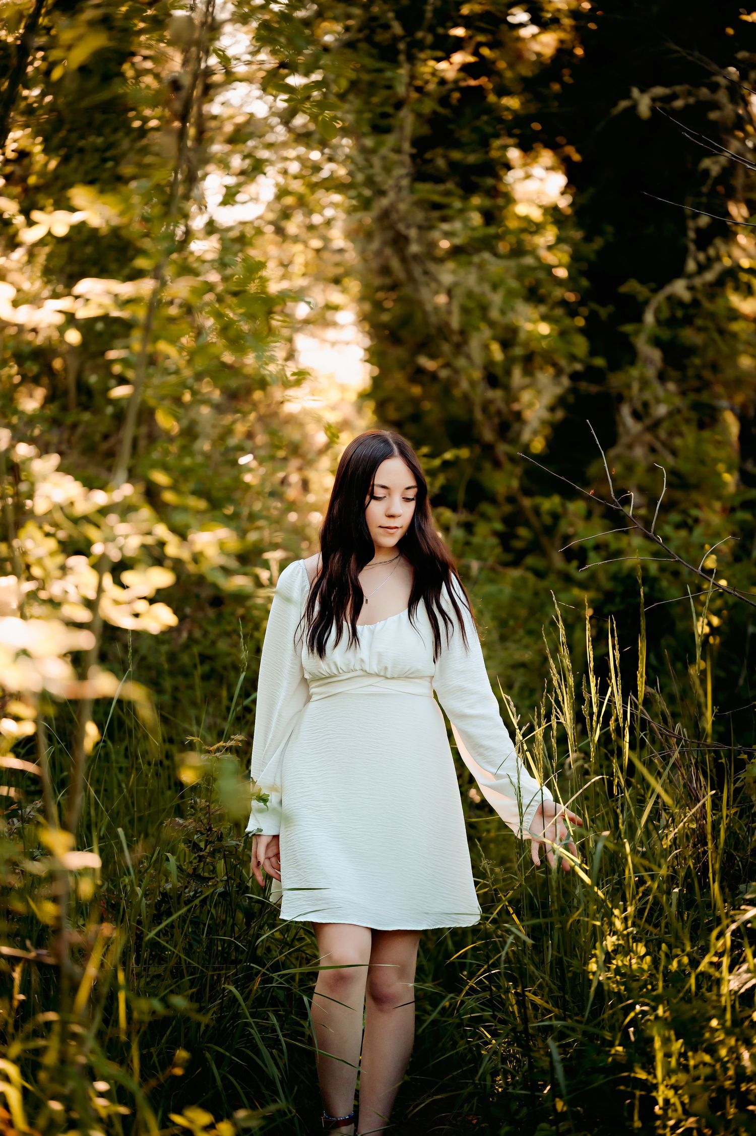 Person in white peasant top poses in tall summer grass during golden hour.