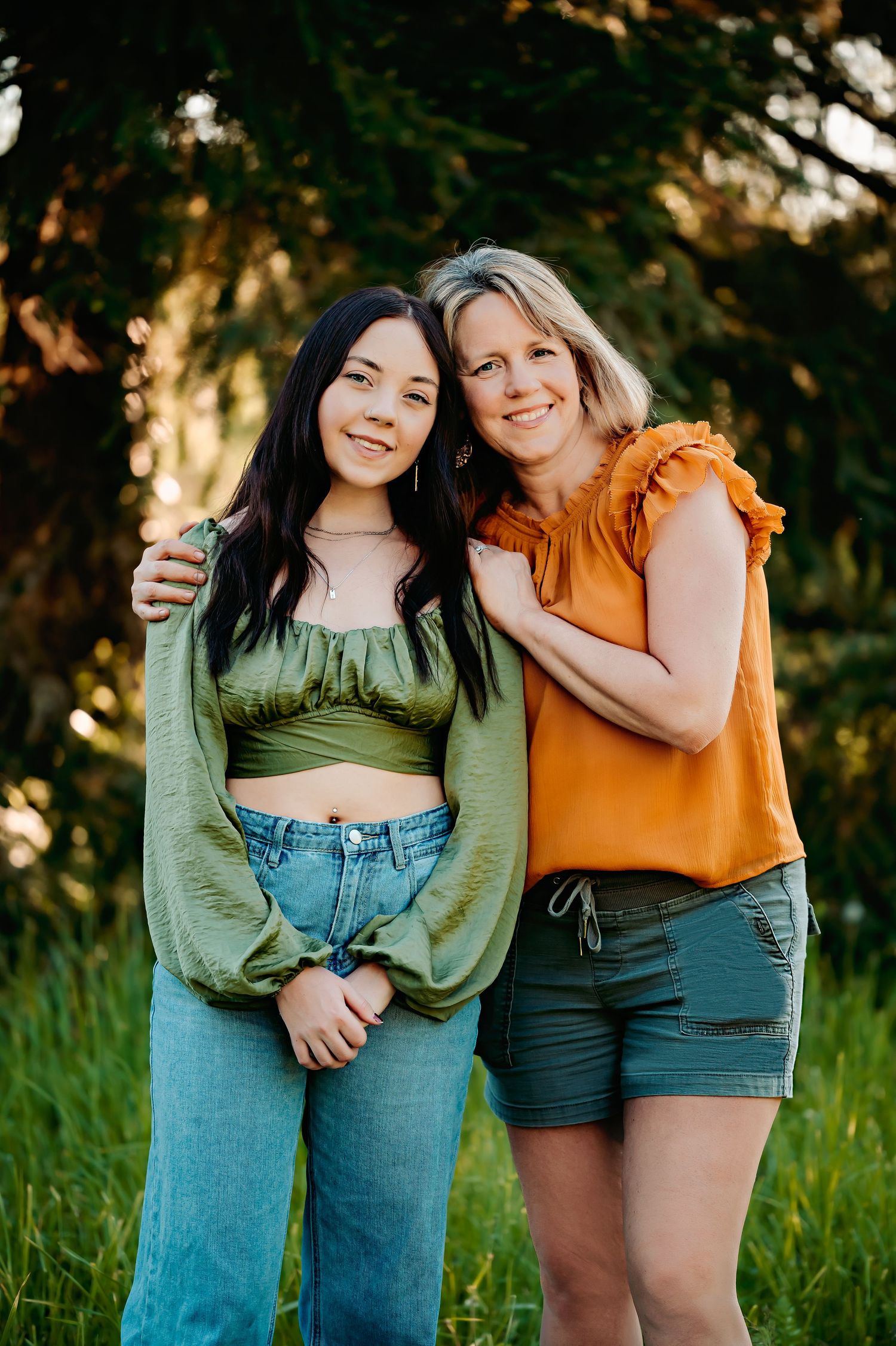 Two friends in casual summer outfits embracing outdoors in green field.