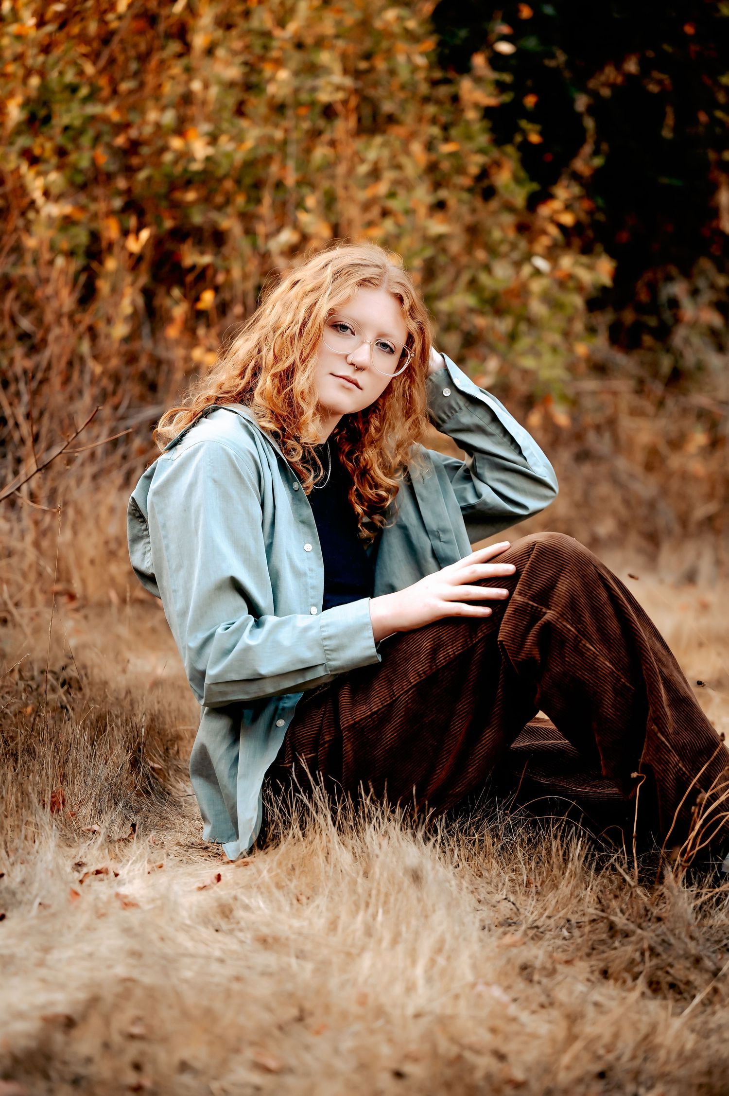 Person in denim jacket lying in autumn grass during golden hour outdoor portrait session.