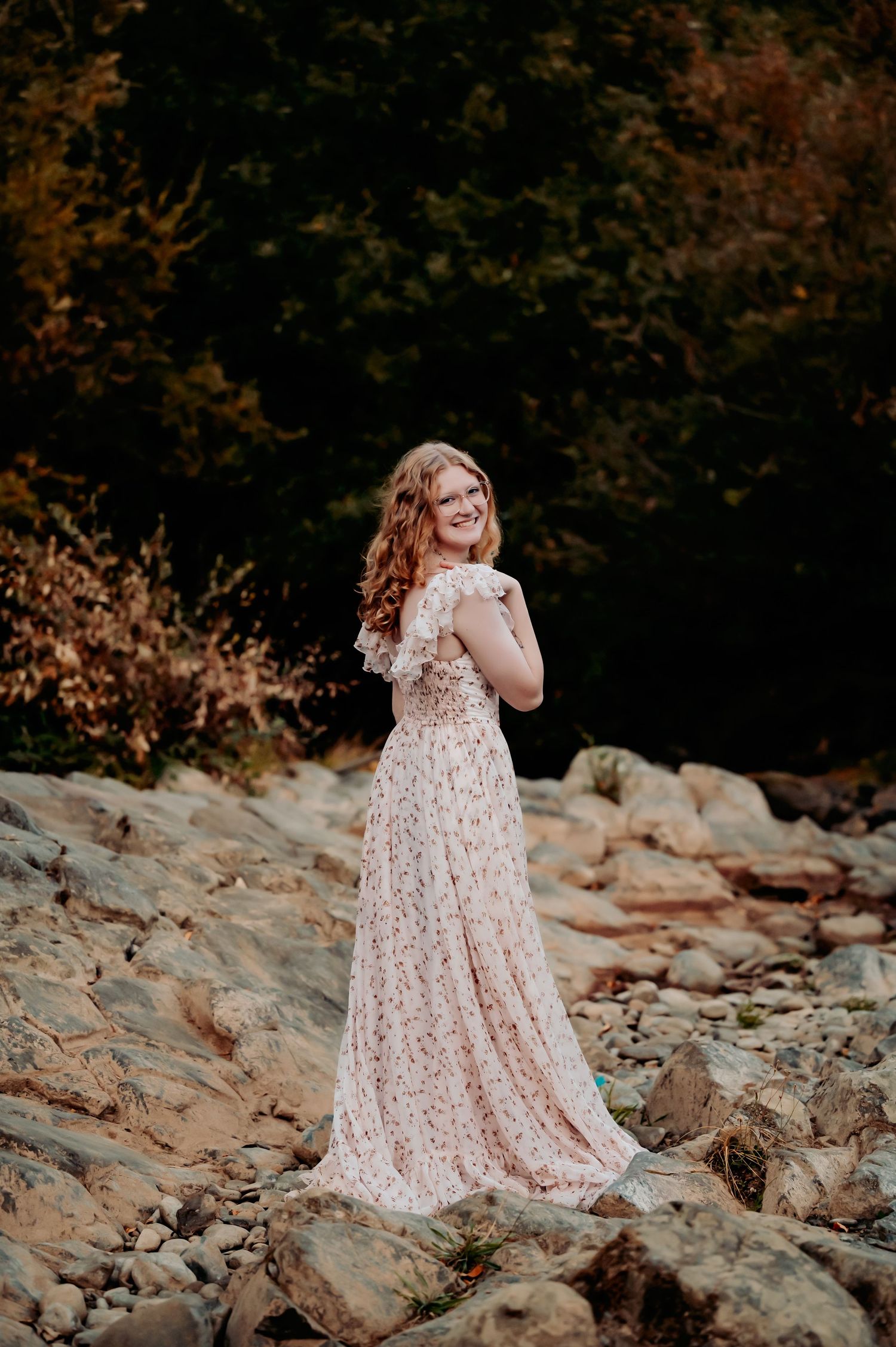 Someone in a flowing lace dress poses on rocky terrain during sunset.