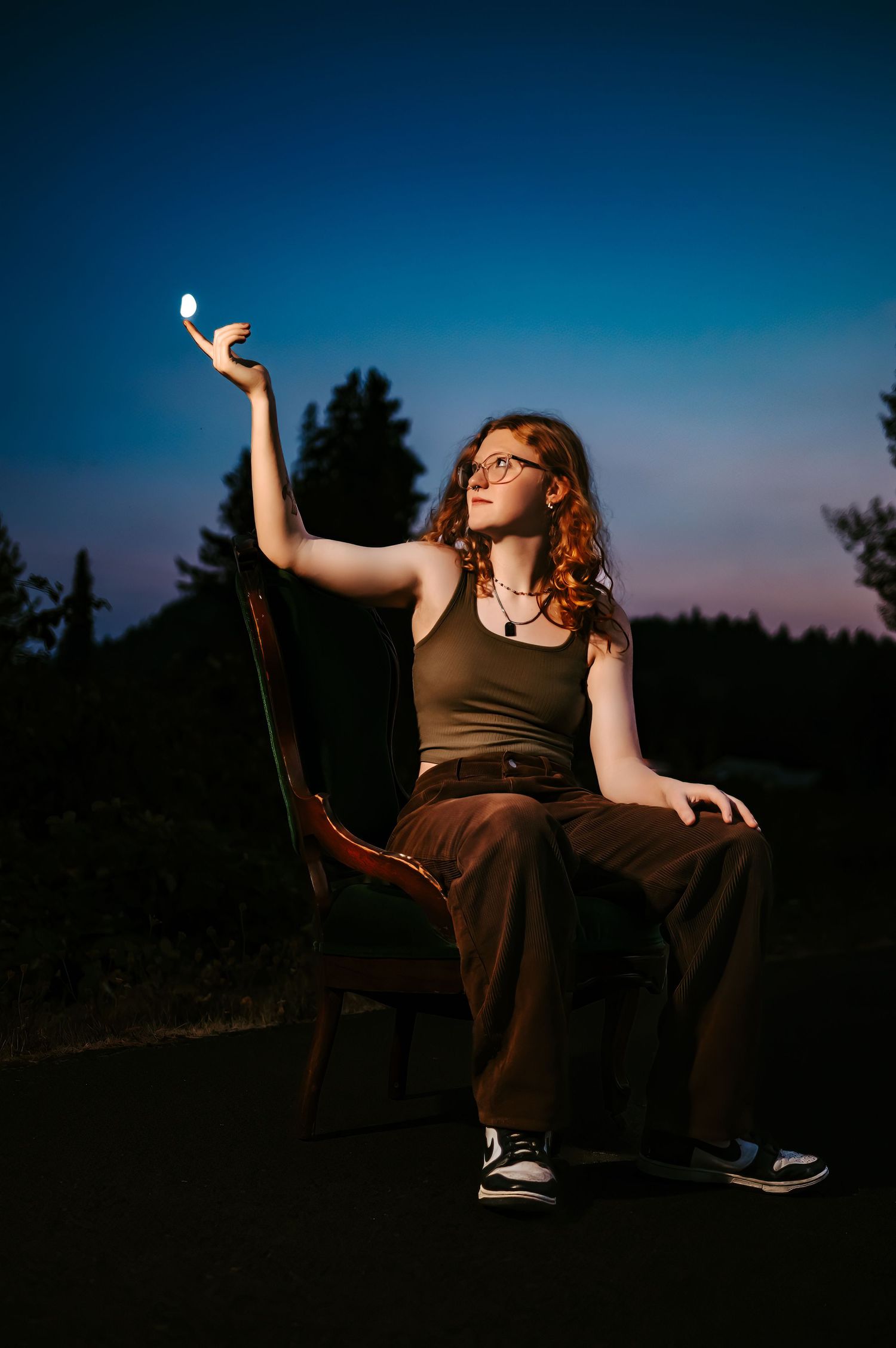 Artistic portrait of someone holding a light in a brown outfit against a deep blue twilight sky.