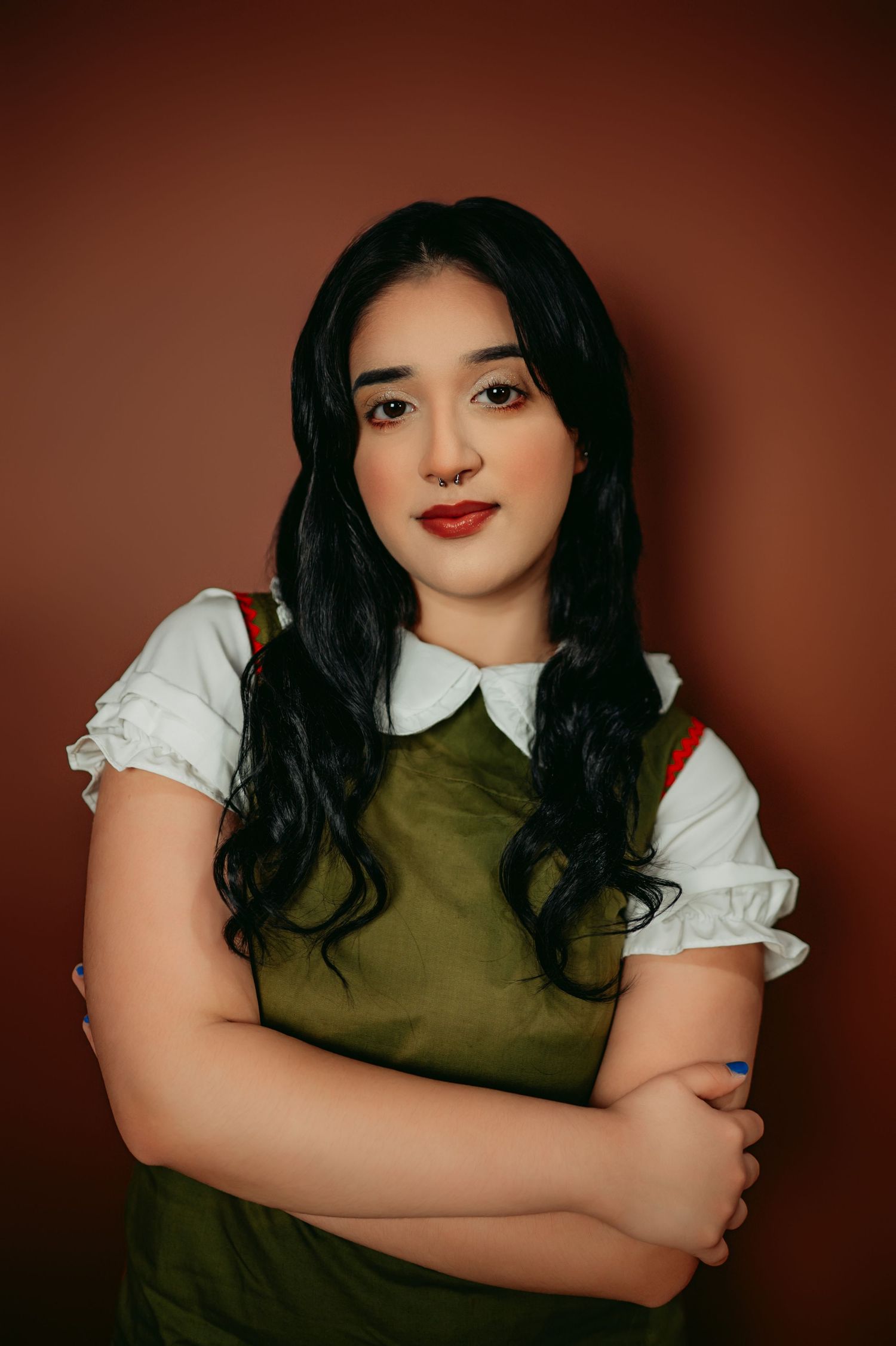 Studio portrait in olive green dress and white blouse against brown background.