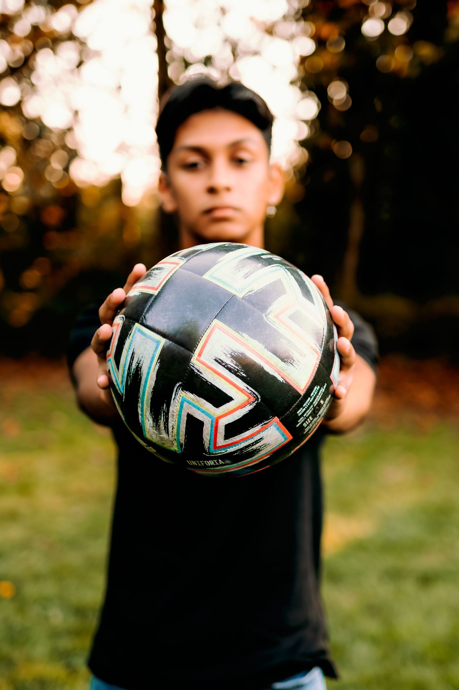 Person holding soccer ball in black shirt against autumn sunset background.