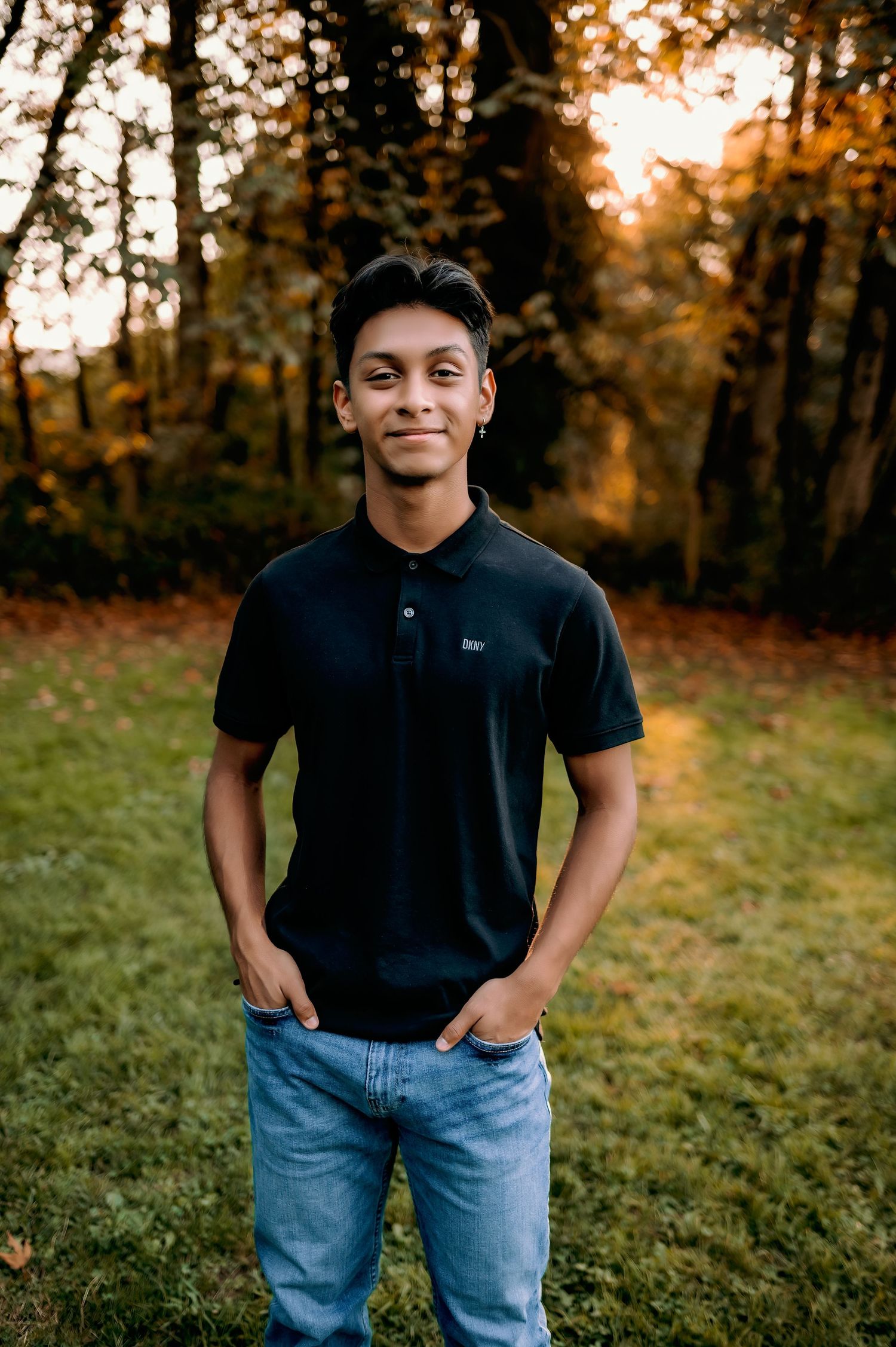 Person in black polo shirt and jeans smiling during golden hour portrait session.