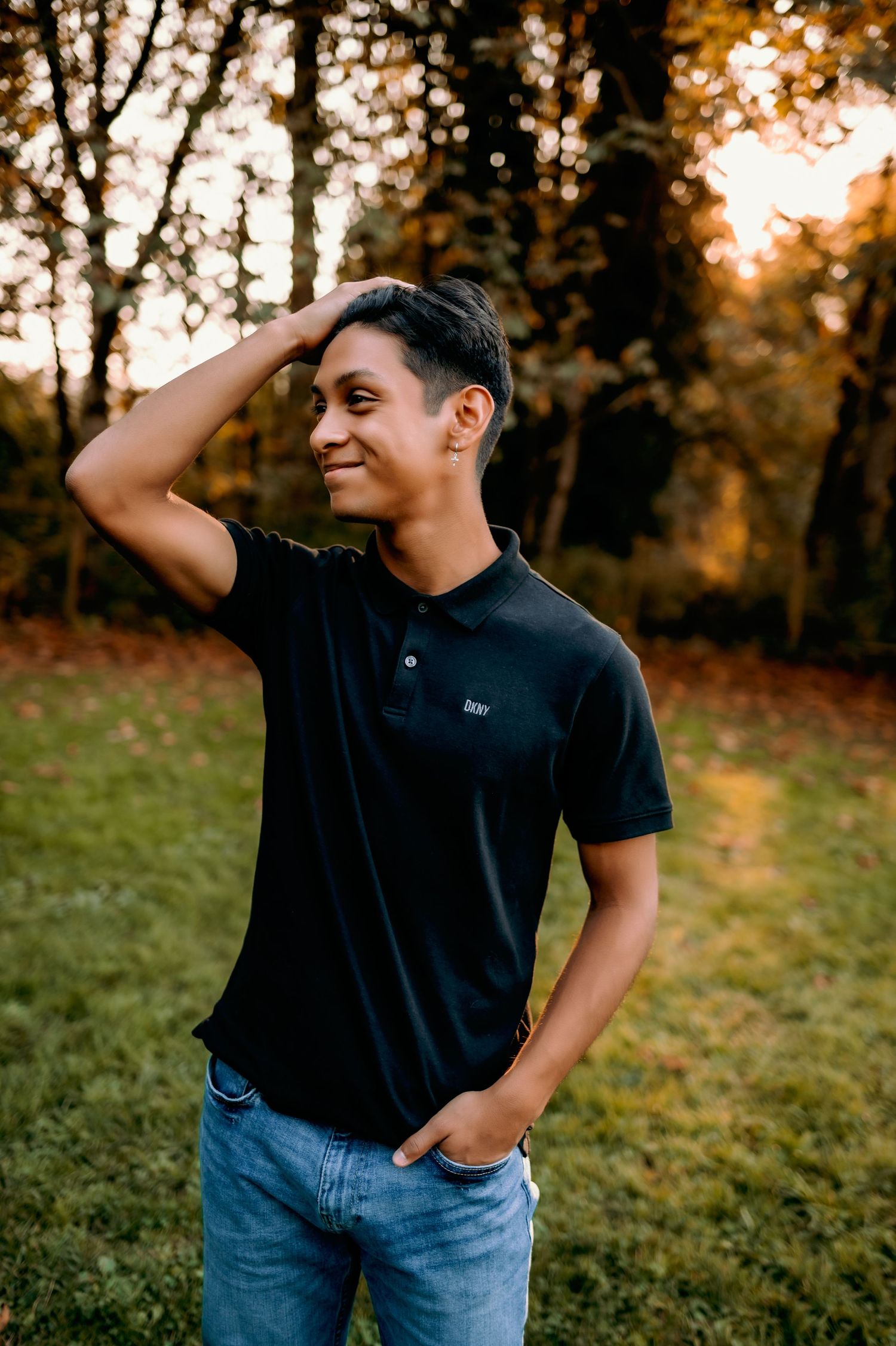 Person in black polo and jeans poses outdoors during sunset photo session.