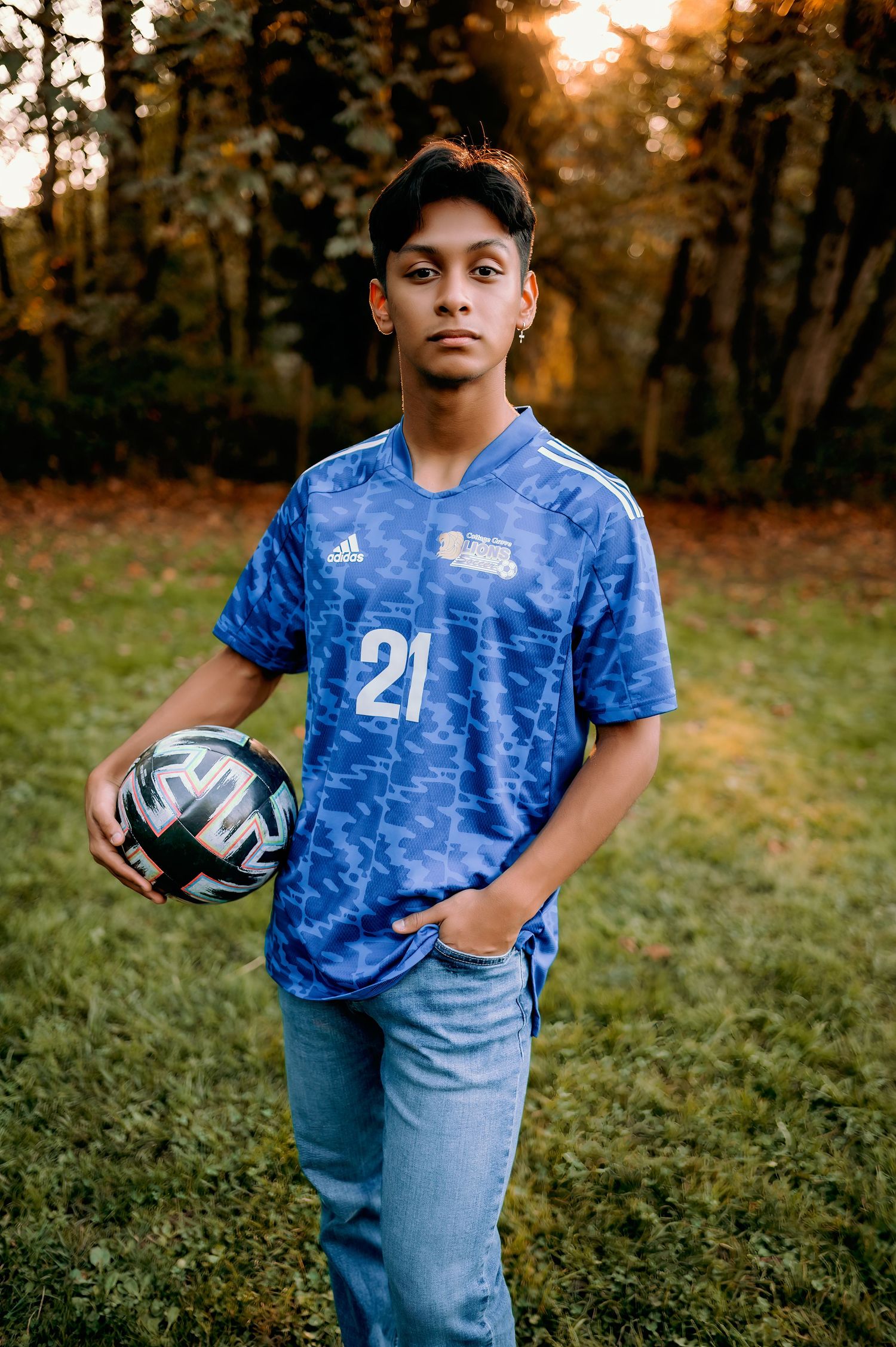 Soccer player in blue jersey and baseball cap holding ball in autumn field.