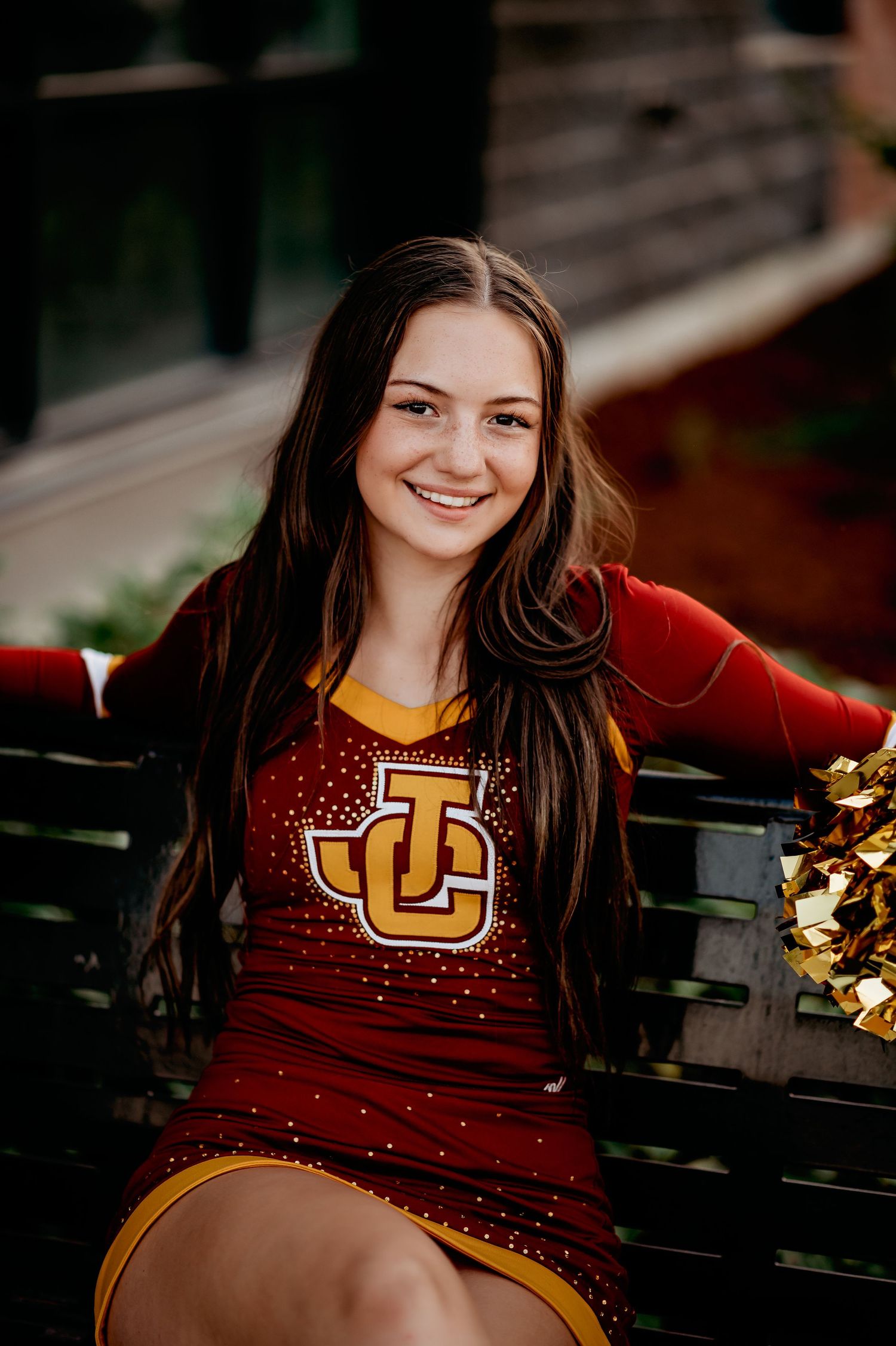 University cheerleader in sparkly maroon uniform sitting on bench with pom poms.