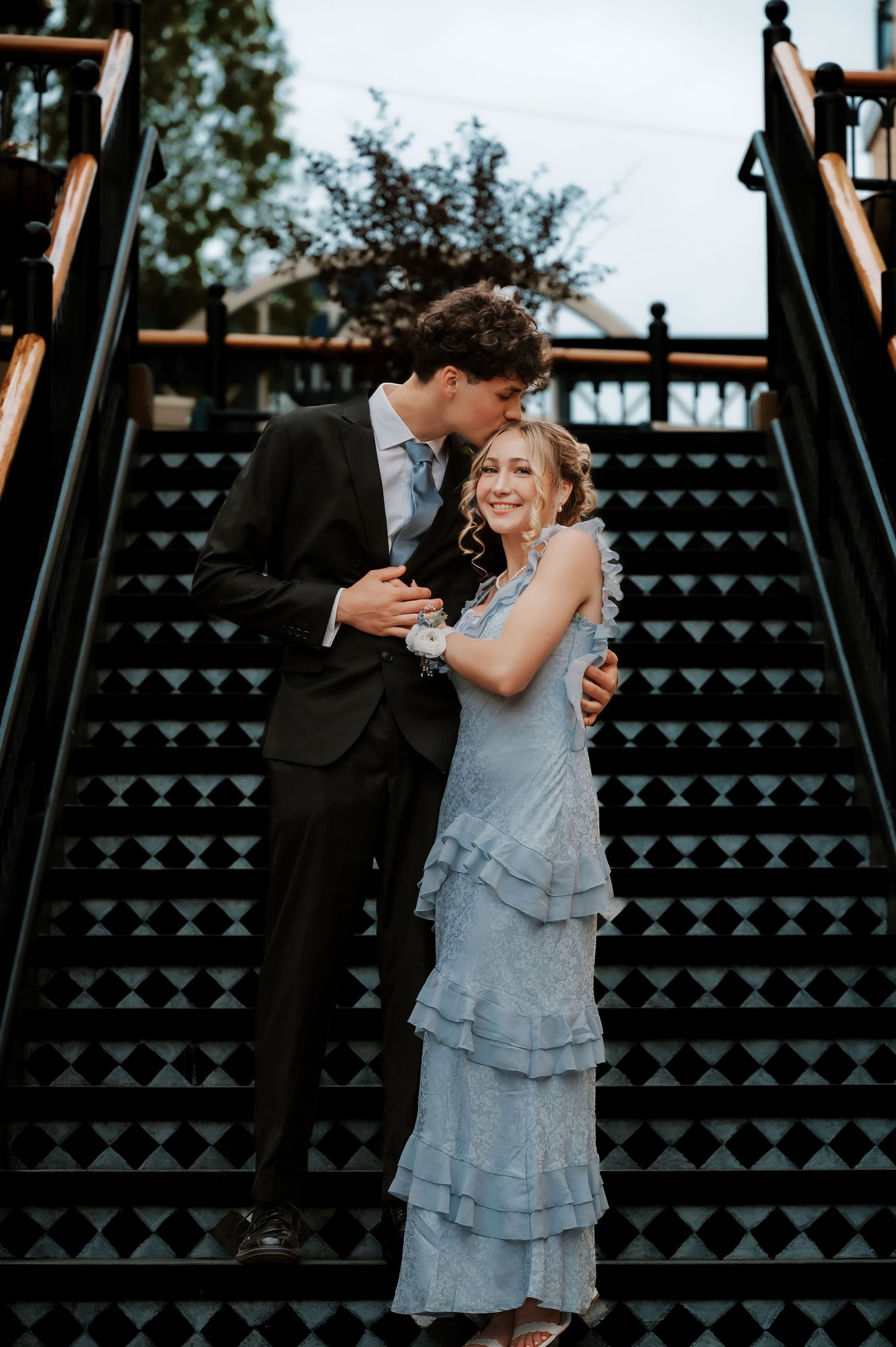 Couple poses playfully on decorative black and white patterned stairs.