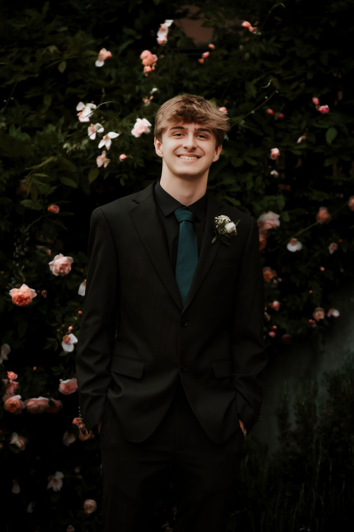 Person in black suit poses against floral background with pink and white roses.