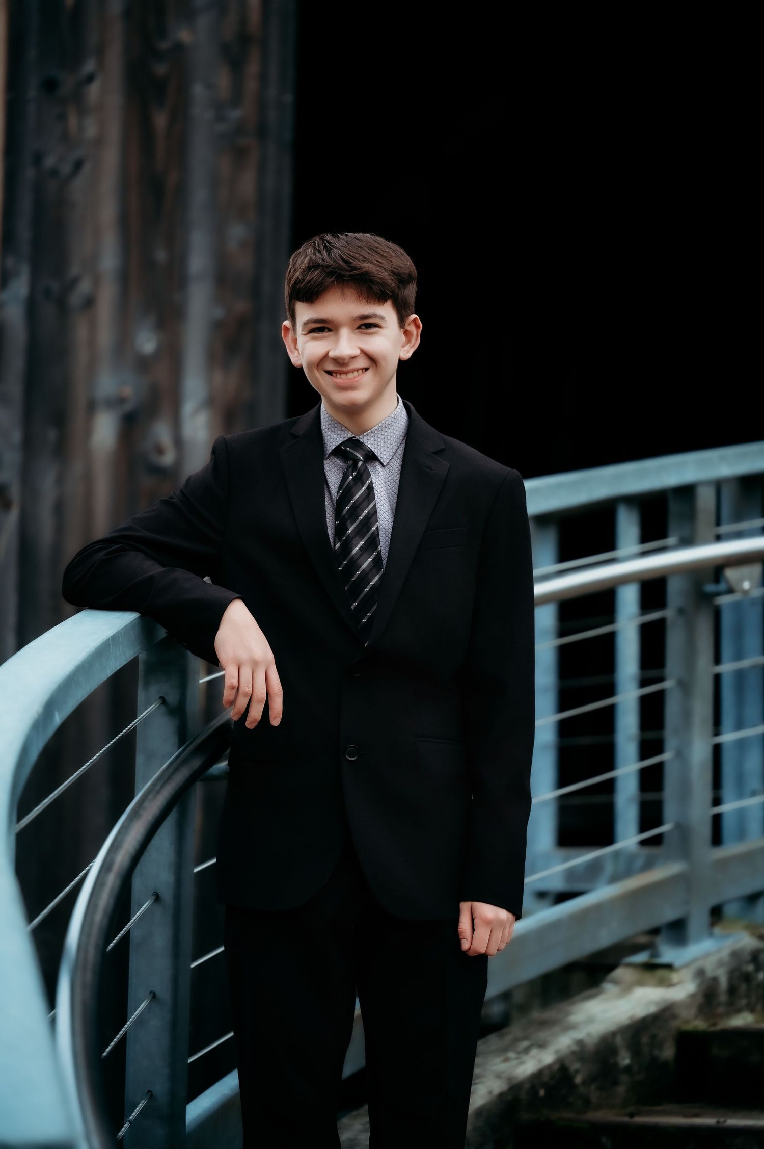 Person in formal suit and striped tie posing by metal railing.
