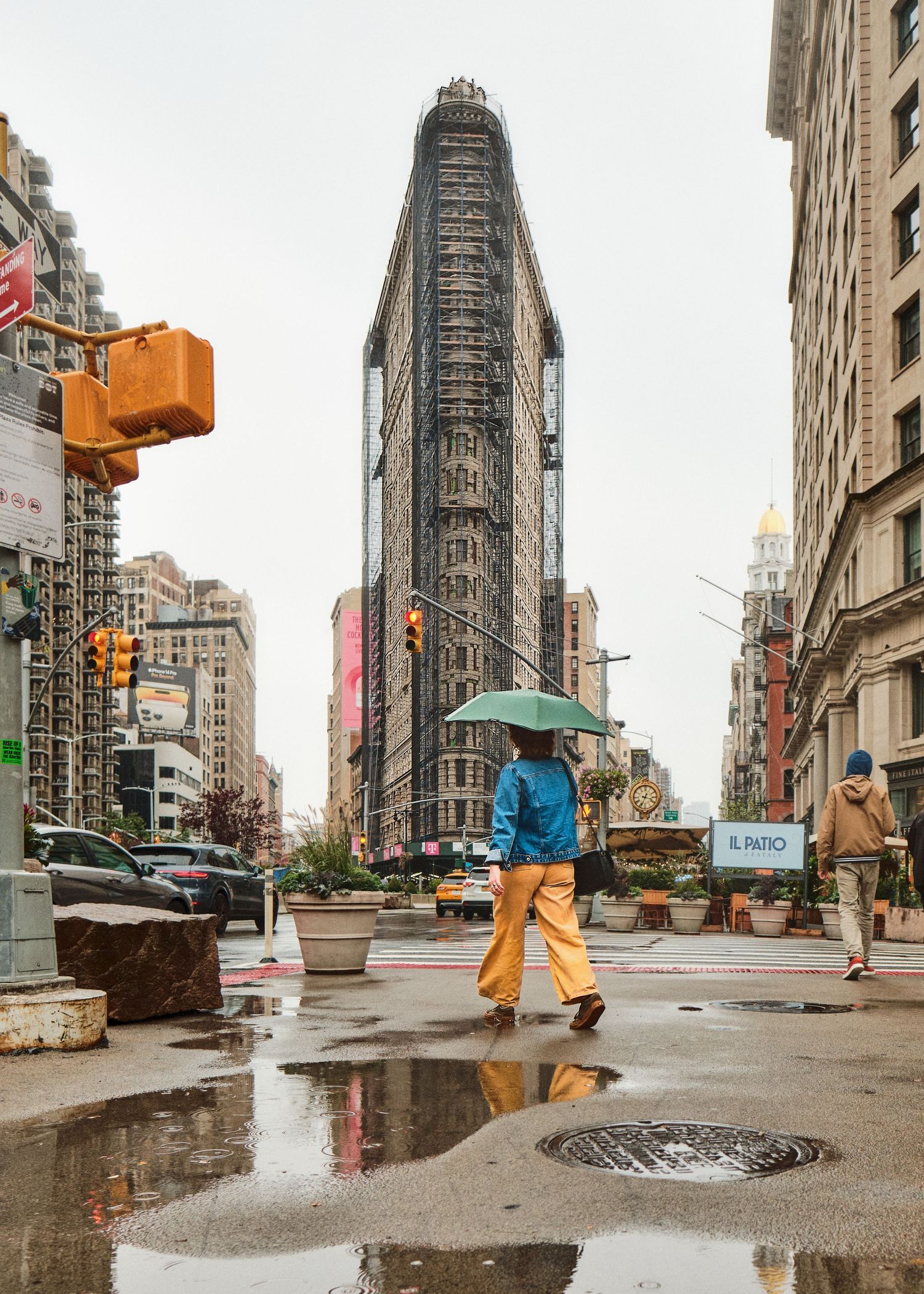 Rainy day view of the historic Flatiron Building in New York City with pedestrians walking by.