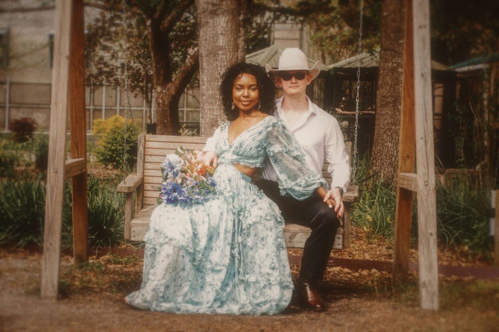 A couple in coordinated blue floral outfits pose together in a romantic garden setting at sunset.