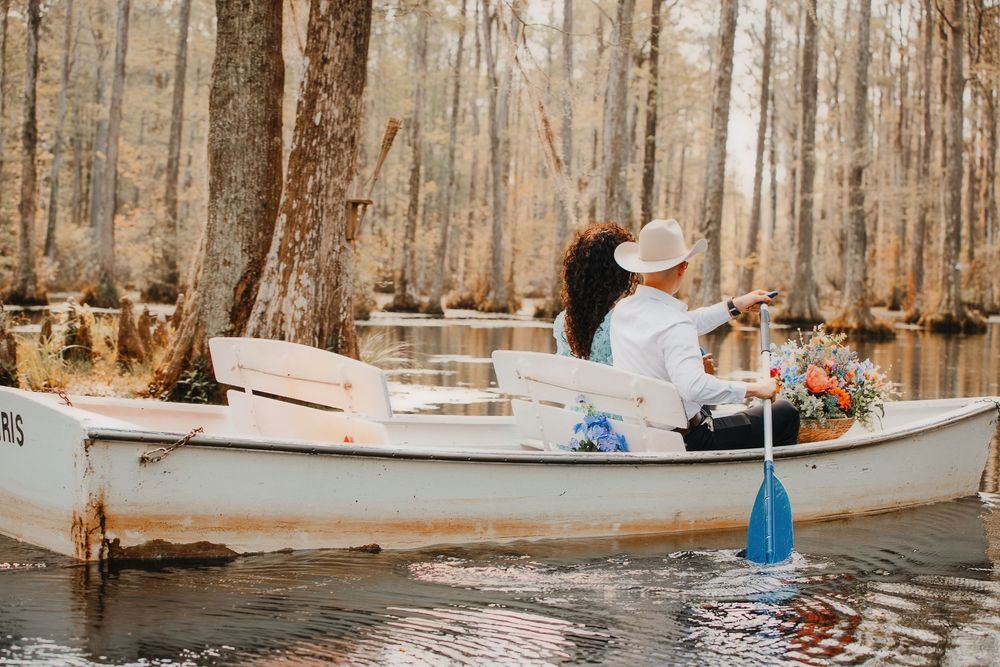 A couple sits together in a white canoe surrounded by cypress trees in a tranquil swamp setting.